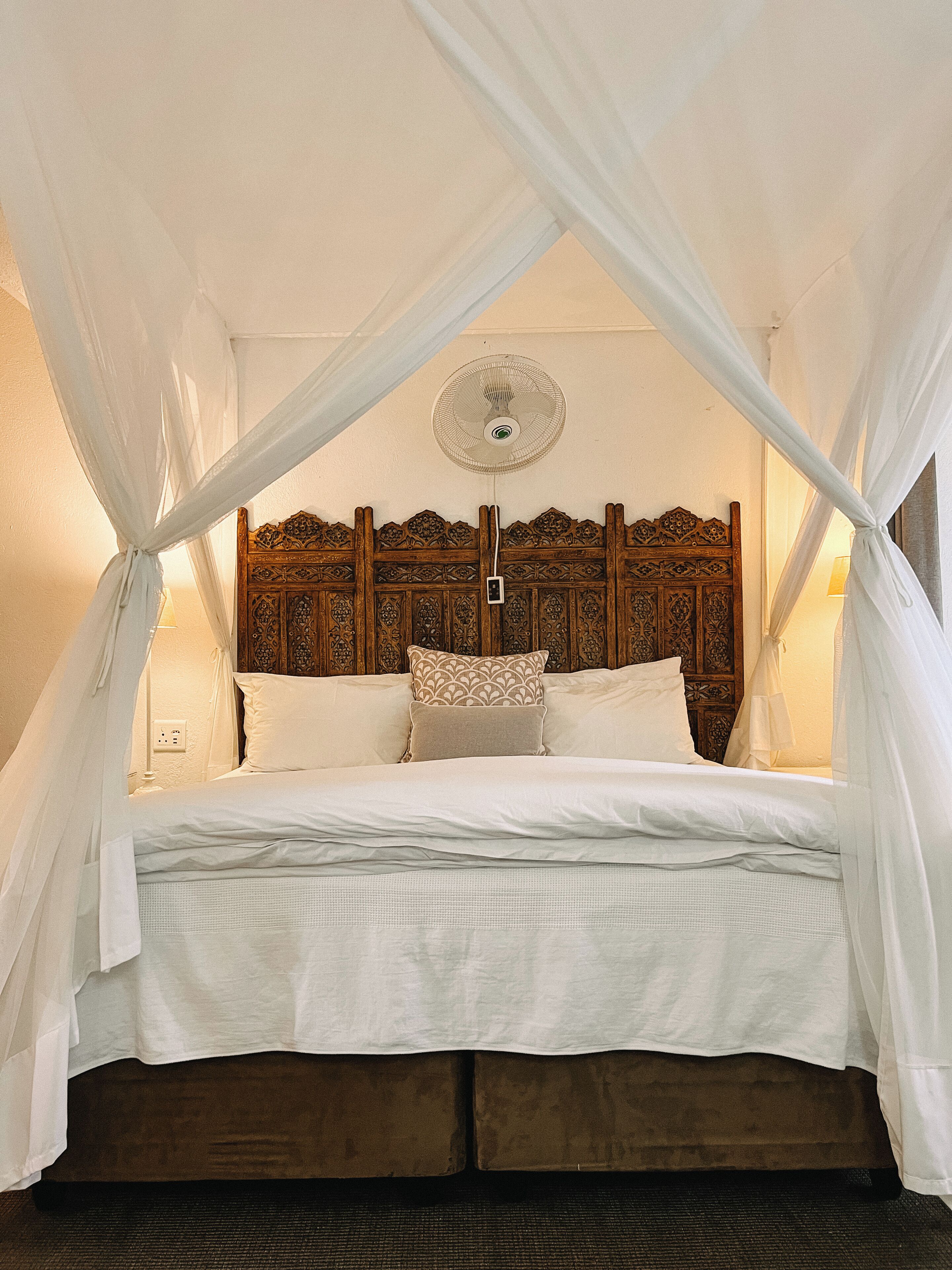 A bed with a canopy, a wooden headboard, and a bedside table with a lamp.