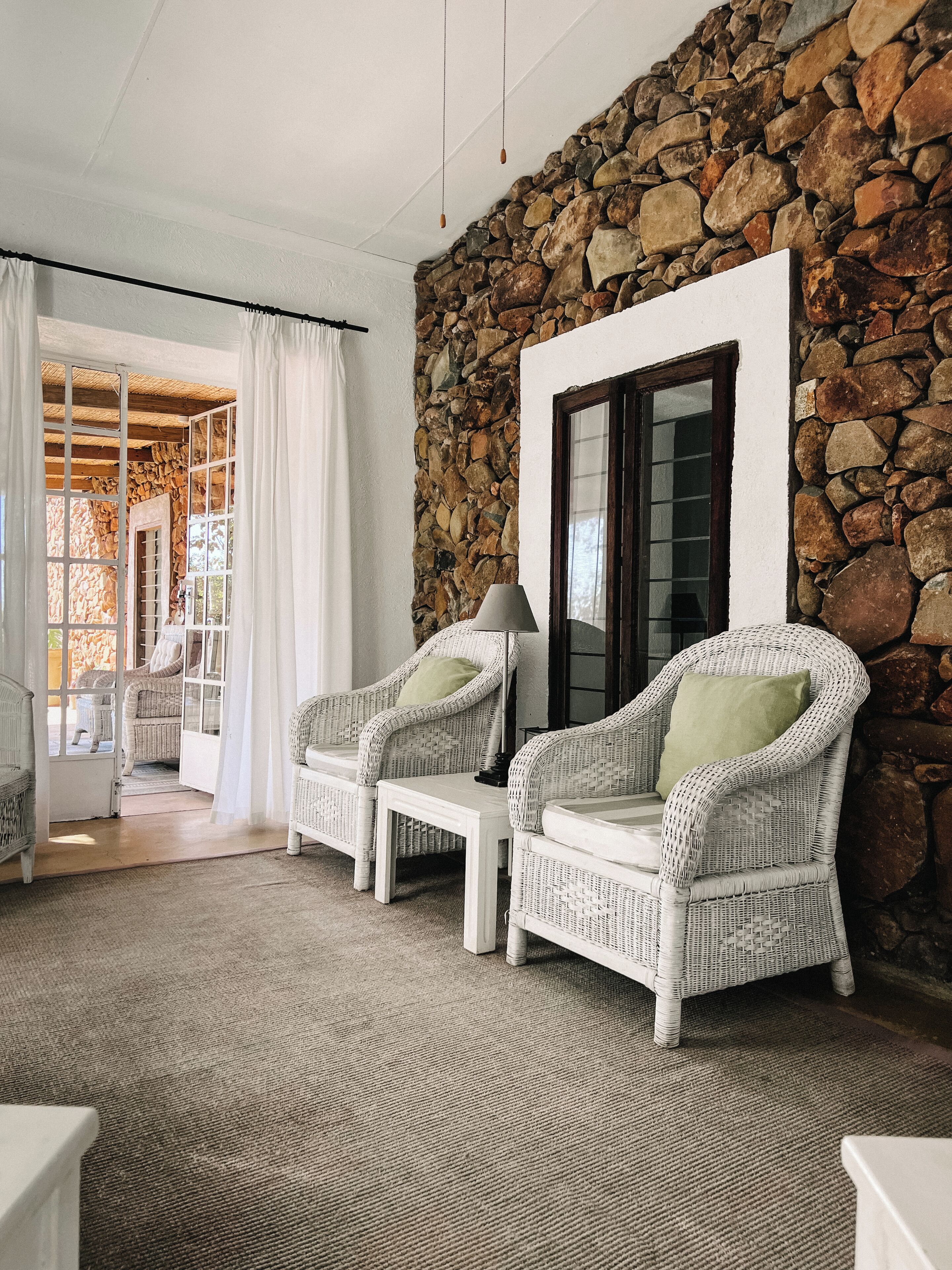A room with wicker furniture, a stone wall, and a view through a glass door.