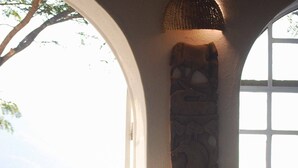 A wicker chair with cushions, a tray with a teapot and cups, and a stone wall with a carved design. - Ashbourne Country Escape (Mbombela)