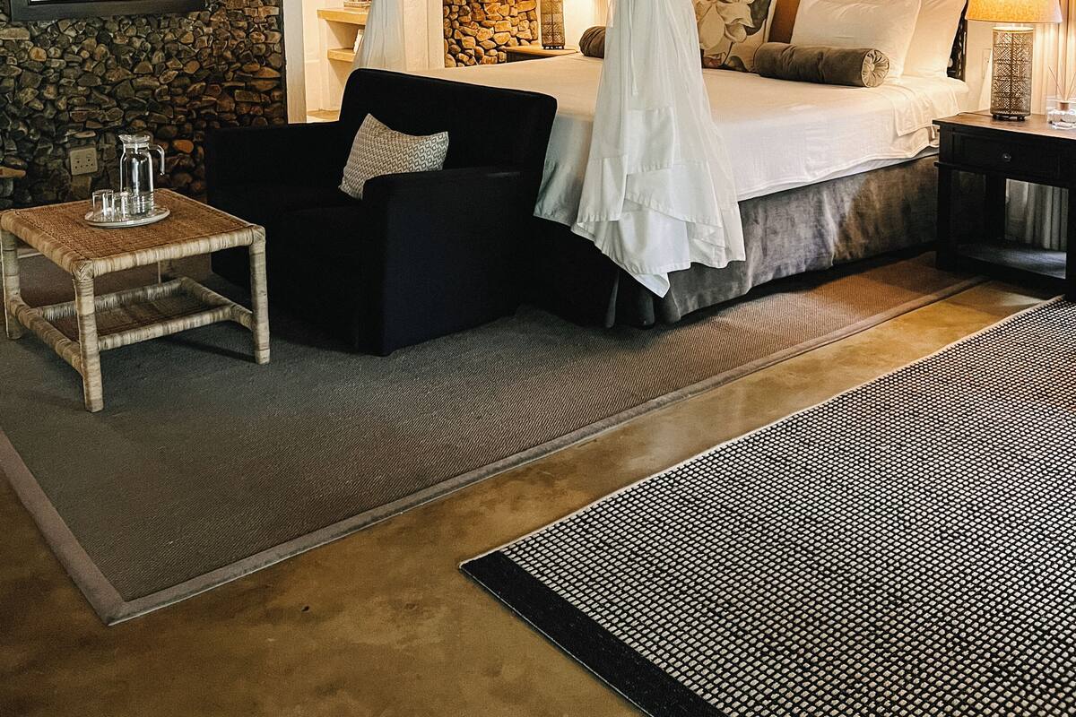 Une chambre à coucher avec un lit à baldaquin, un mur en pierre, une petite table avec une carafe et un canapé noir.
