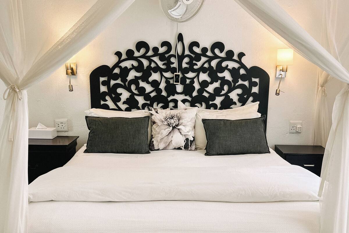 Un lit à baldaquin, une tête de lit décorative, des lampes de chevet et une table de chevet.
