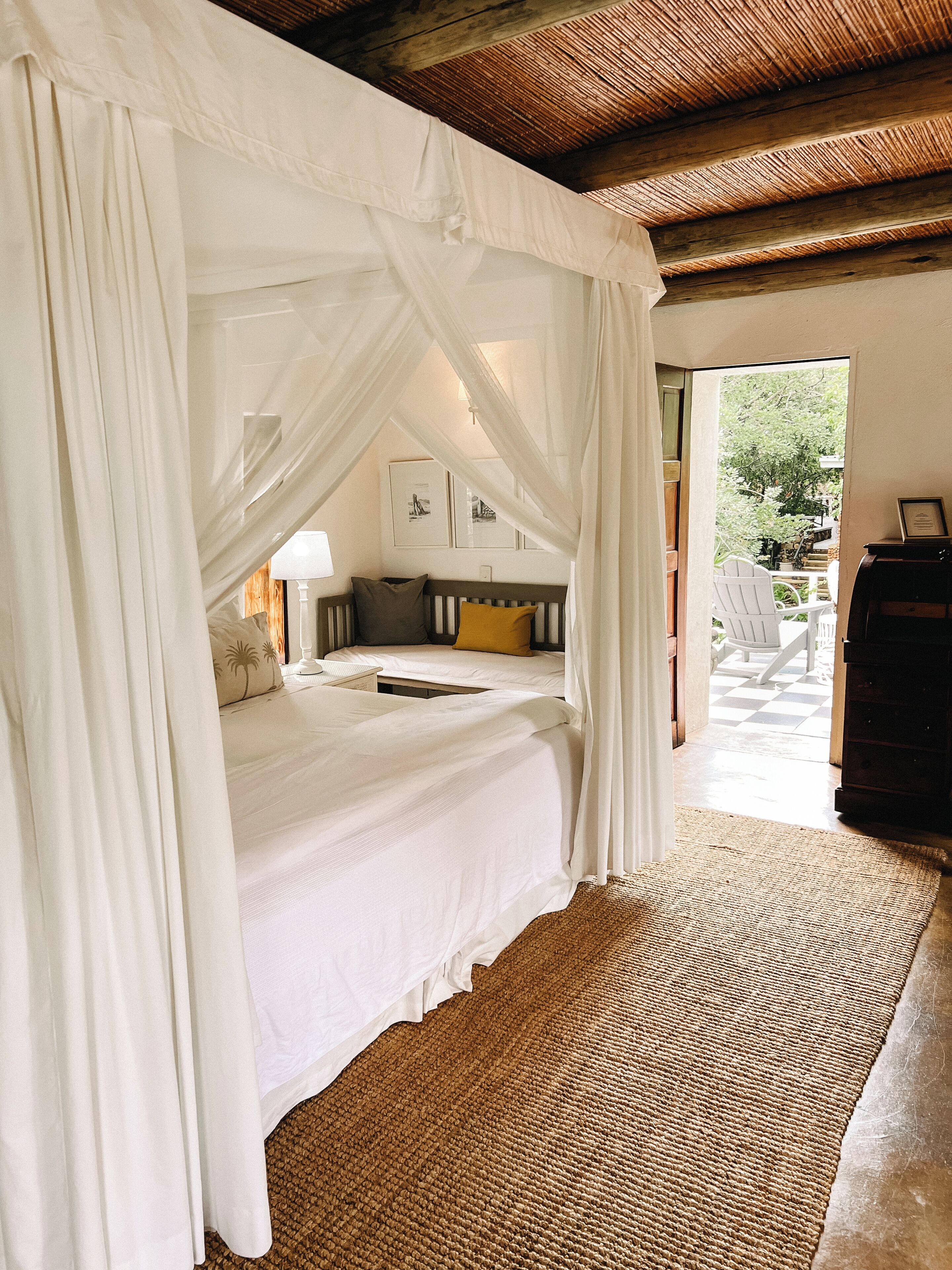 A bedroom with a canopy bed, a wooden floor, and a view of the outside.