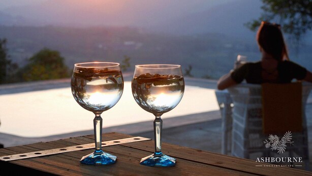Two wine glasses on a wooden table with a scenic view in the background. - Ashbourne Country Escape (Mbombela)