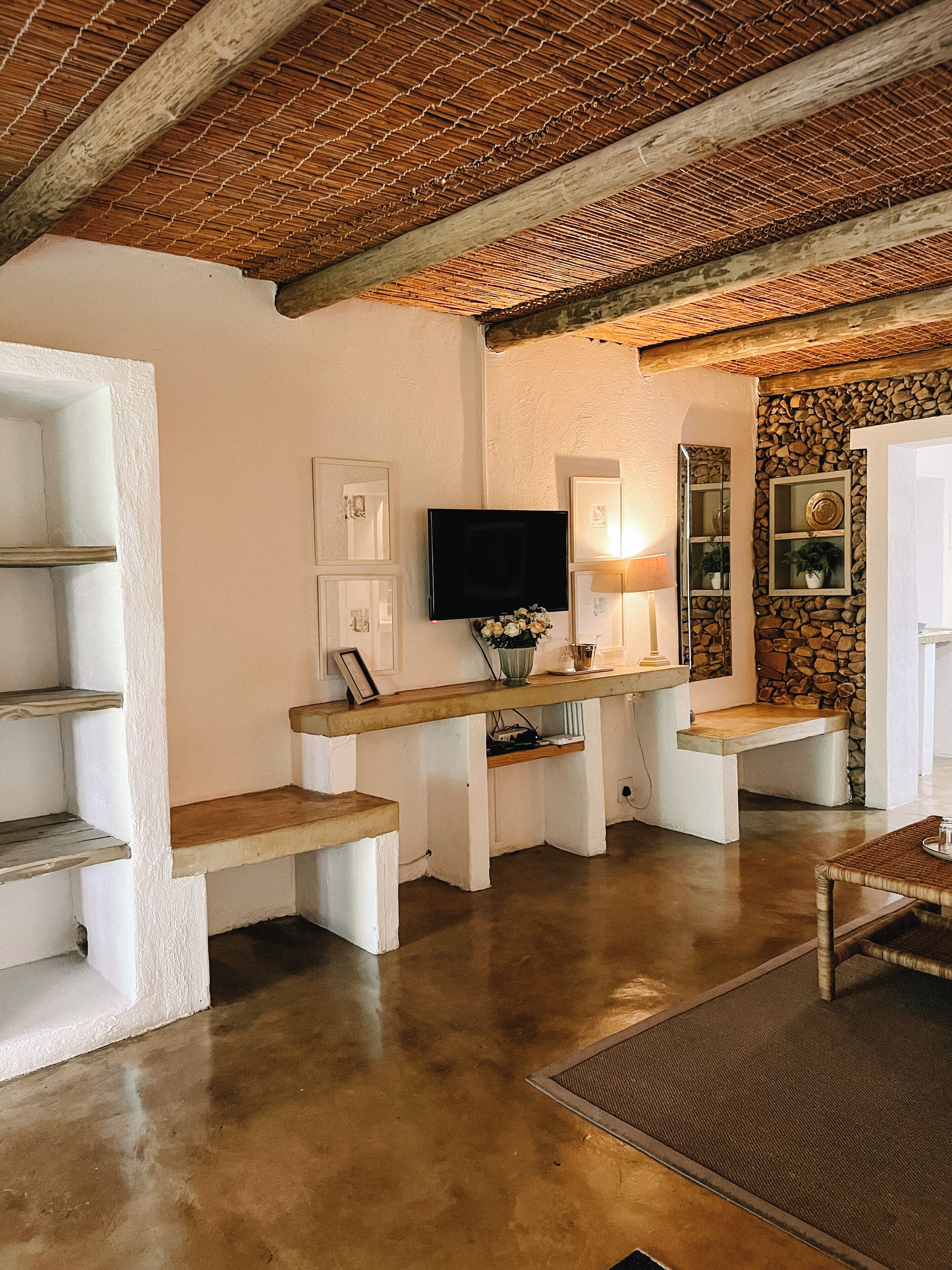 A room with a stone wall, a television mounted on the wall, and a wooden bench.