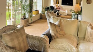 A cozy living room with a sofa, wicker chairs, a TV, and a fireplace. - Ashbourne Country Escape (Mbombela)