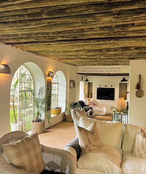 A cozy living room with a sofa, wicker chairs, a TV, and a fireplace. - Ashbourne Country Escape (Mbombela)