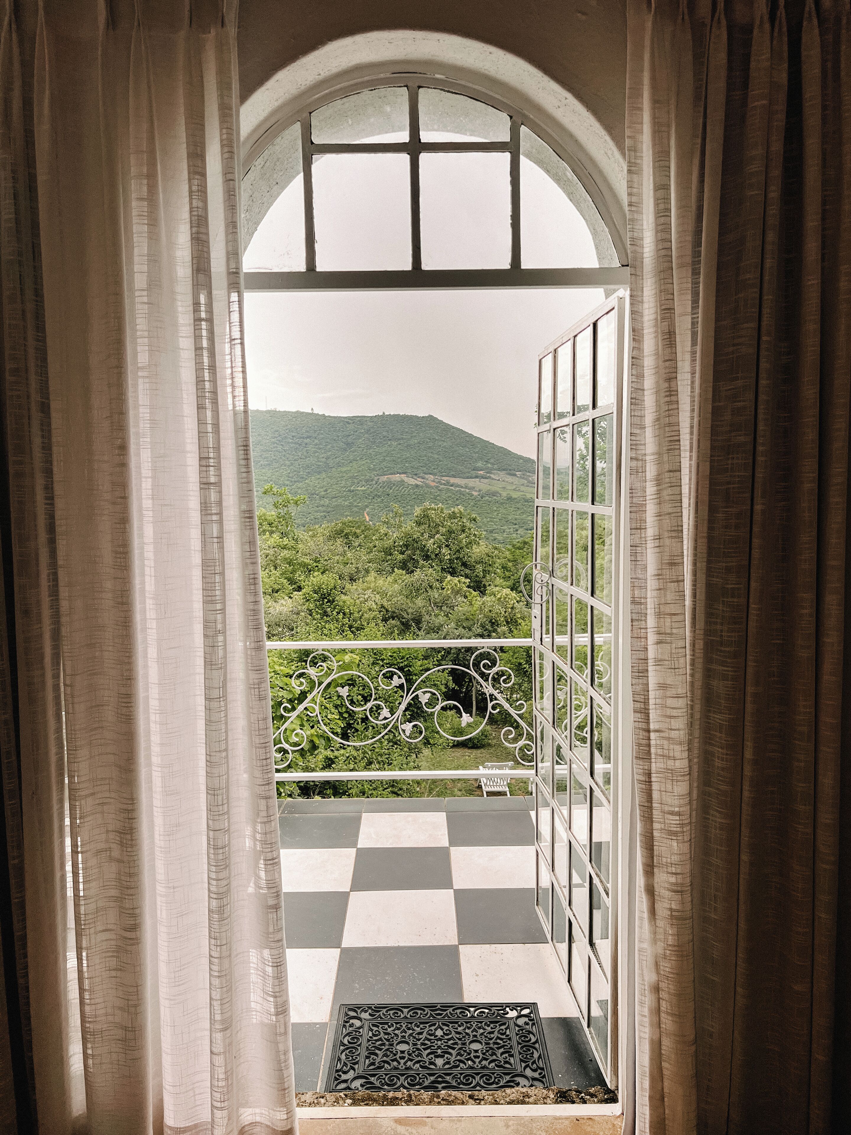 An open balcony with a checkered floor, a metal railing, and a view of a green landscape.