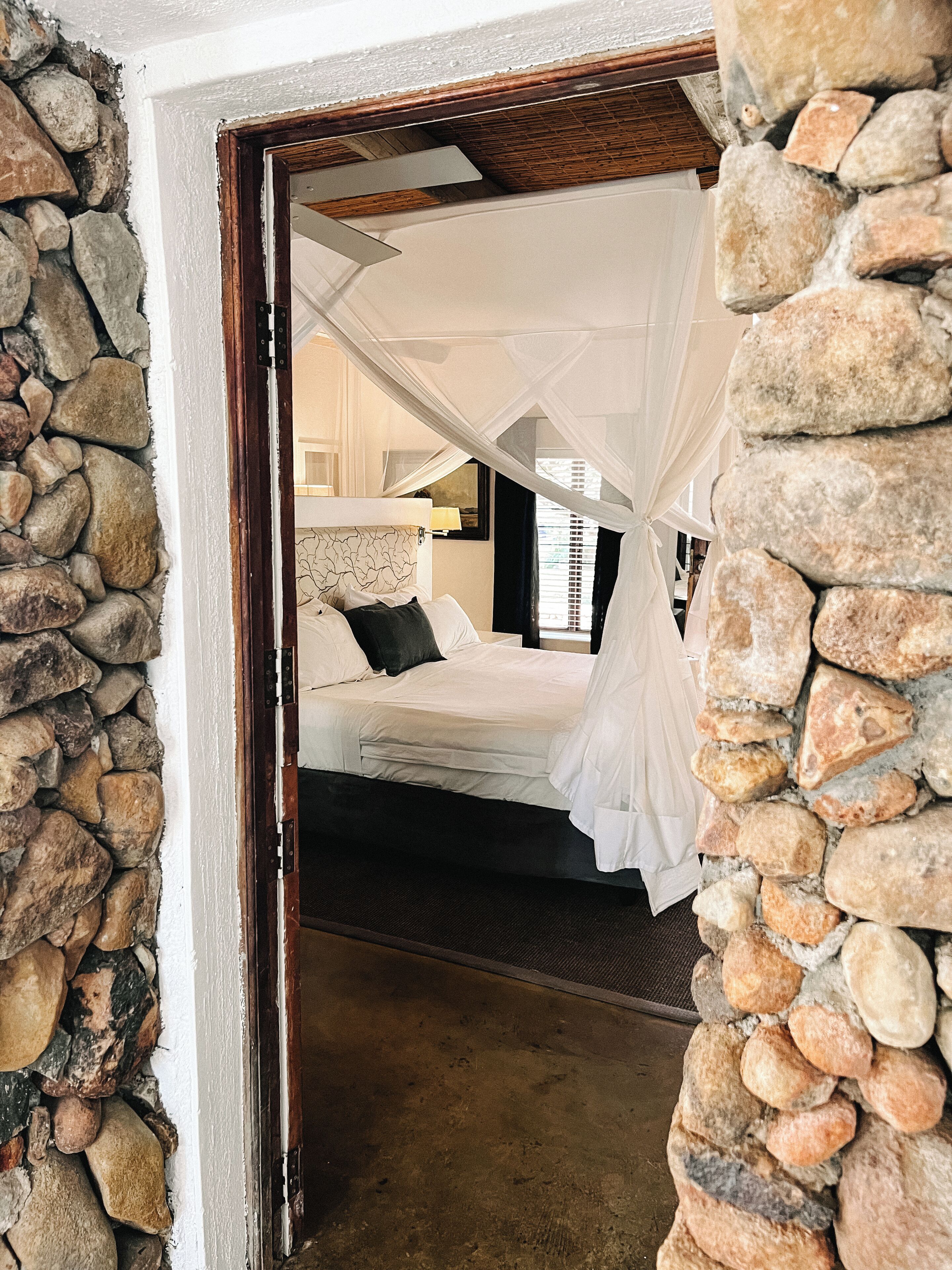 A bedroom with a stone wall, a bed with white bedding, and a canopy.