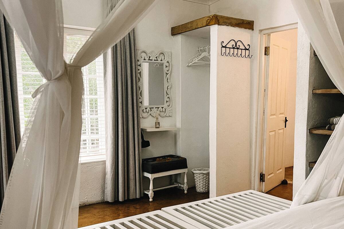 Une chambre à coucher avec un lit à baldaquin, une coiffeuse avec un miroir, une porte et une fenêtre avec des rideaux.