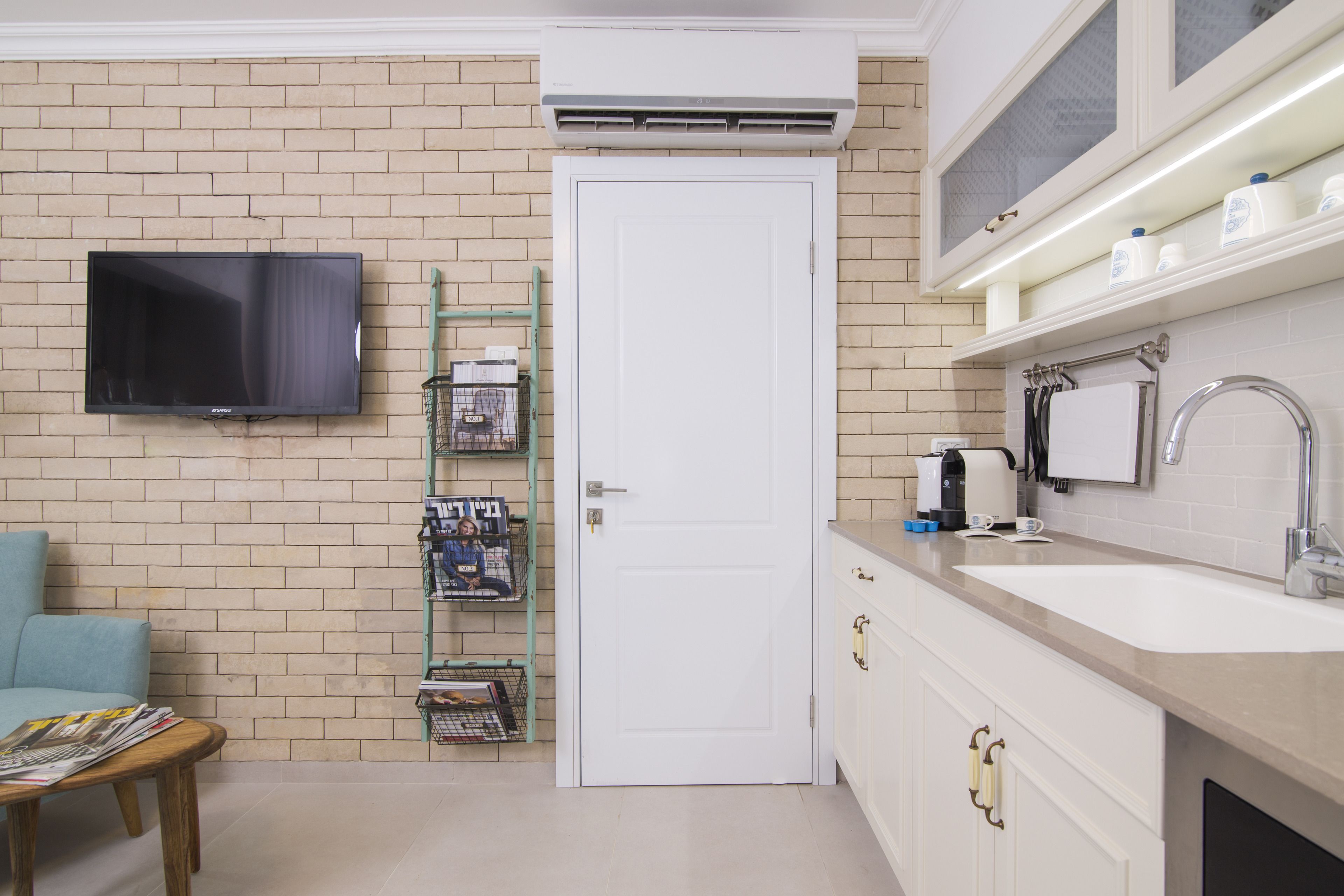 A kitchen with a white door, a flat-screen TV mounted on the wall, a coffee maker, and a sink.