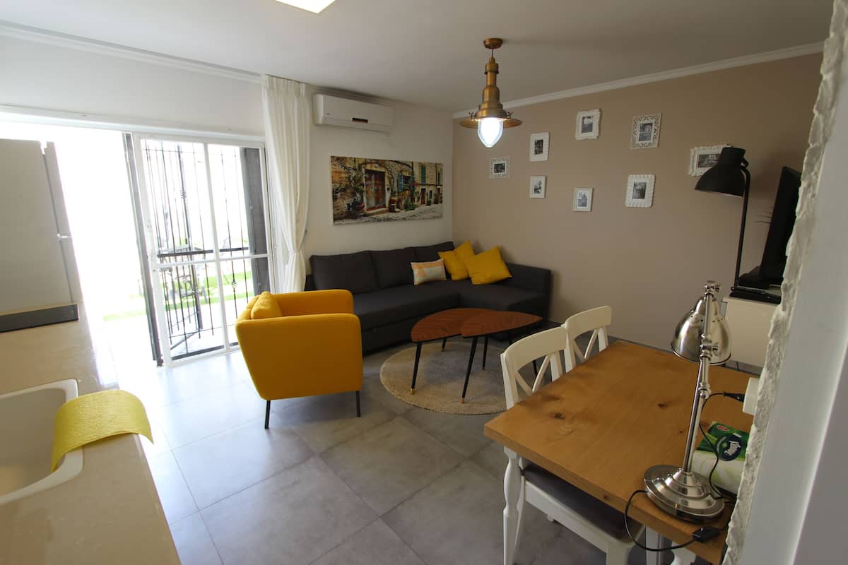 A modern living room with a sofa, yellow armchair, round coffee table, and a dining table with a lamp.