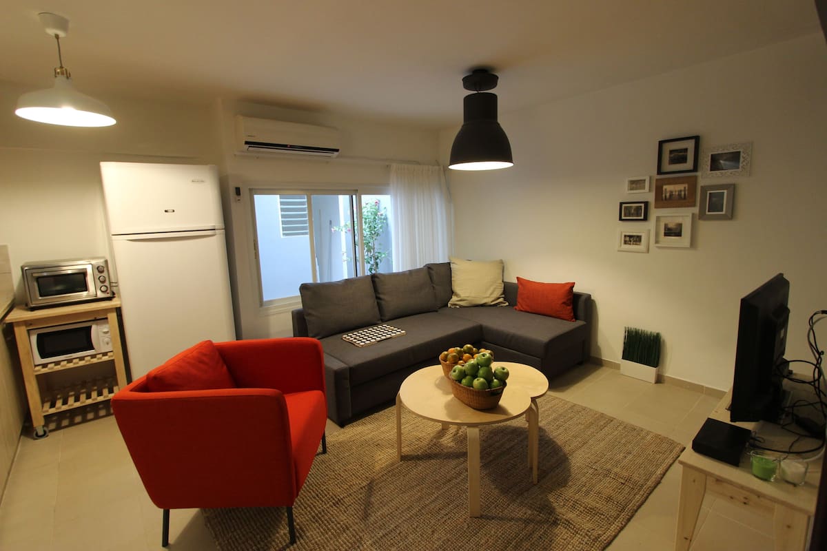 A living room with a sofa, a red armchair, a small table with fruit, a television, and a microwave.