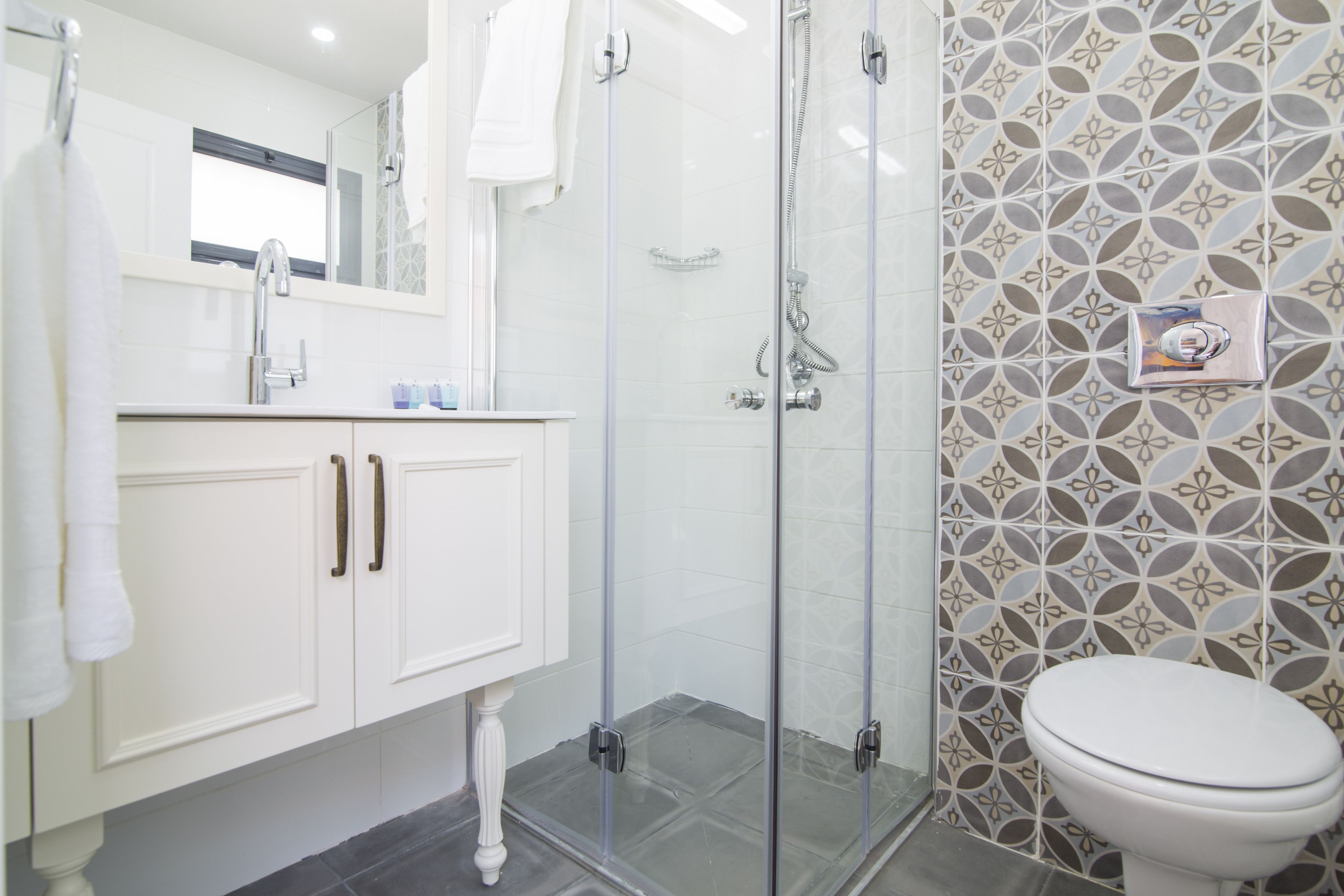 Un baño con cabina de ducha de vidrio, inodoro blanco y azulejos con diseño en las paredes.