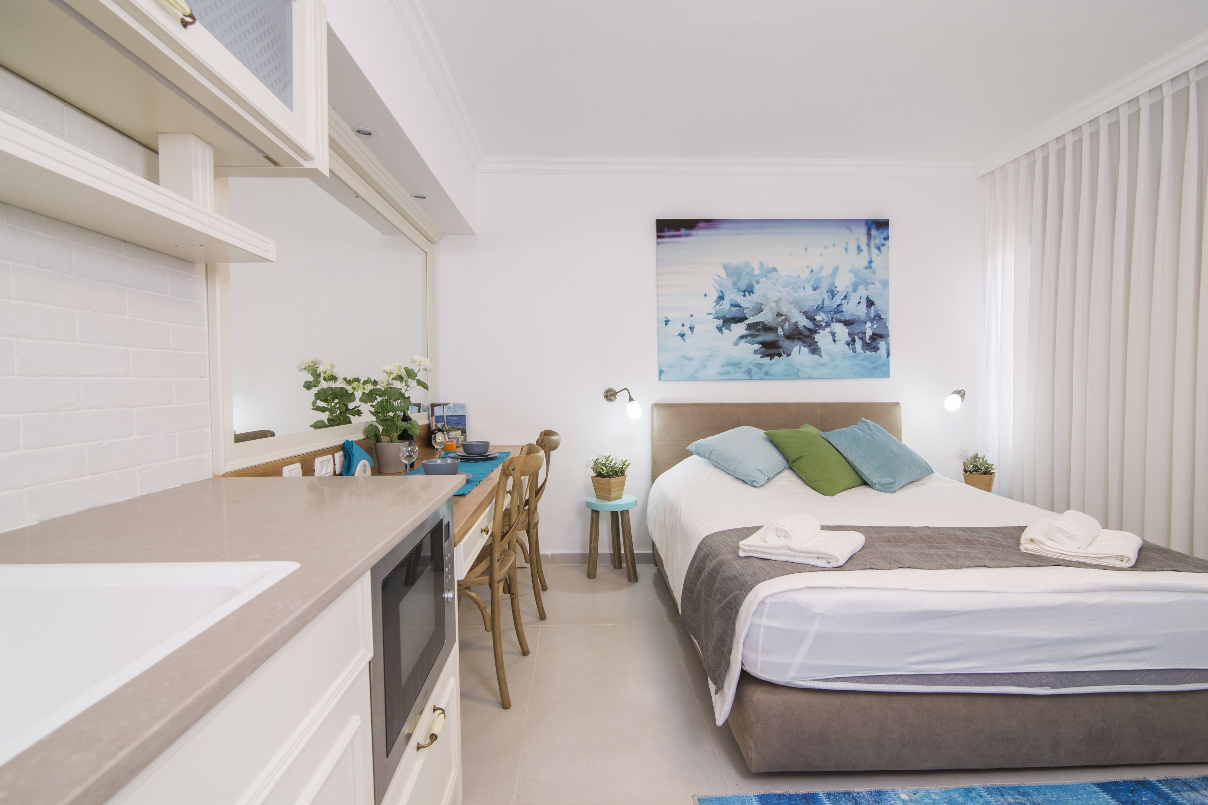 Une chambre d’hôtel moderne dotée d’une kitchenette, d’un lit donnant sur la ville et d’un tableau accroché au mur.