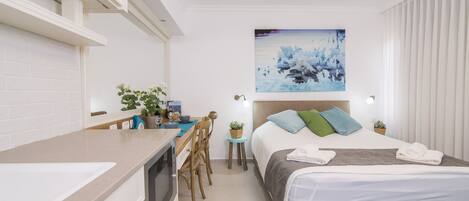 Une chambre d’hôtel moderne dotée d’une kitchenette, d’un lit donnant sur la ville et d’un tableau accroché au mur.