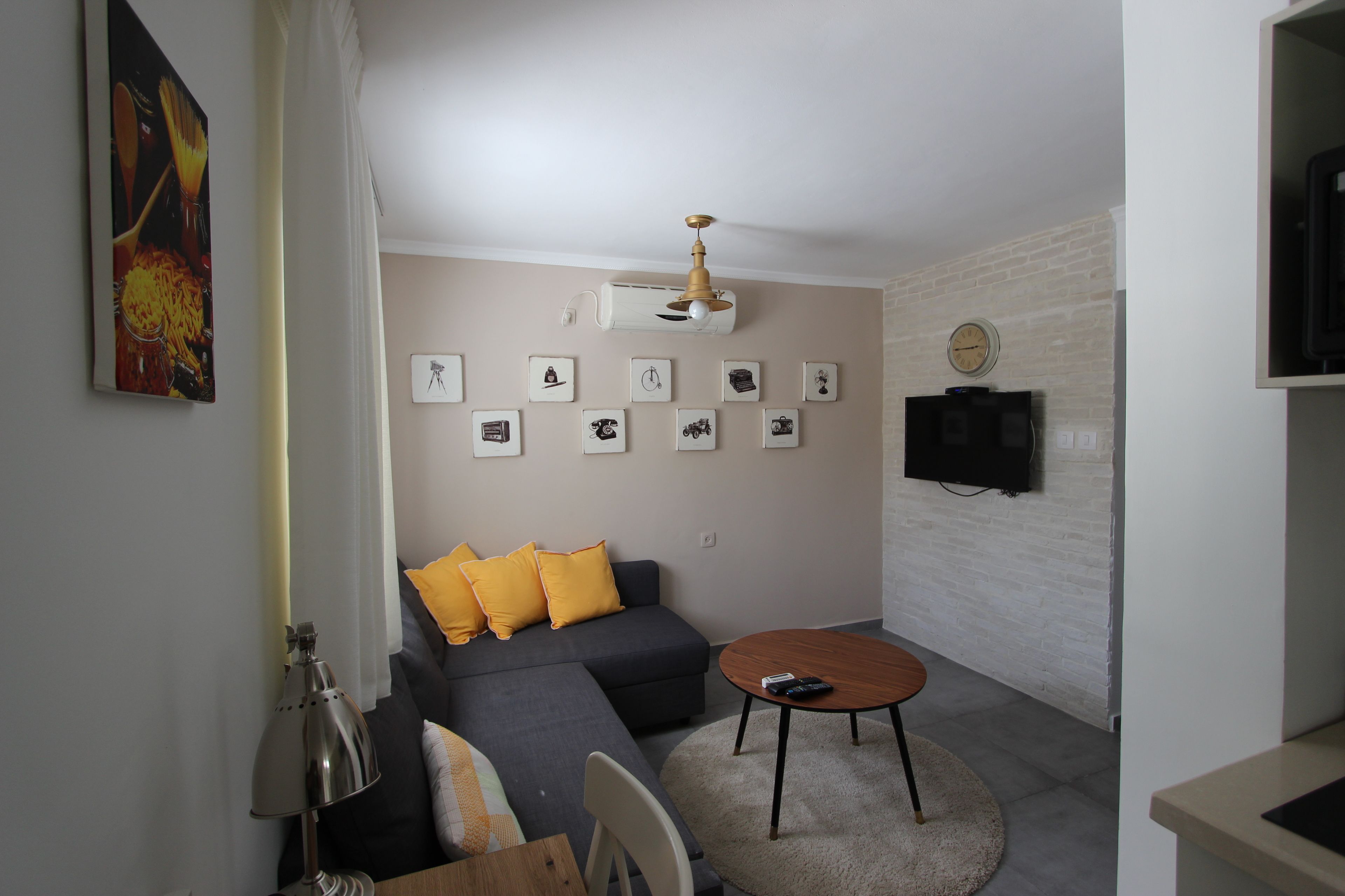 Una sala de estar moderna con un sofá gris, cojines amarillos, una mesa redonda de centro y un televisor montado.