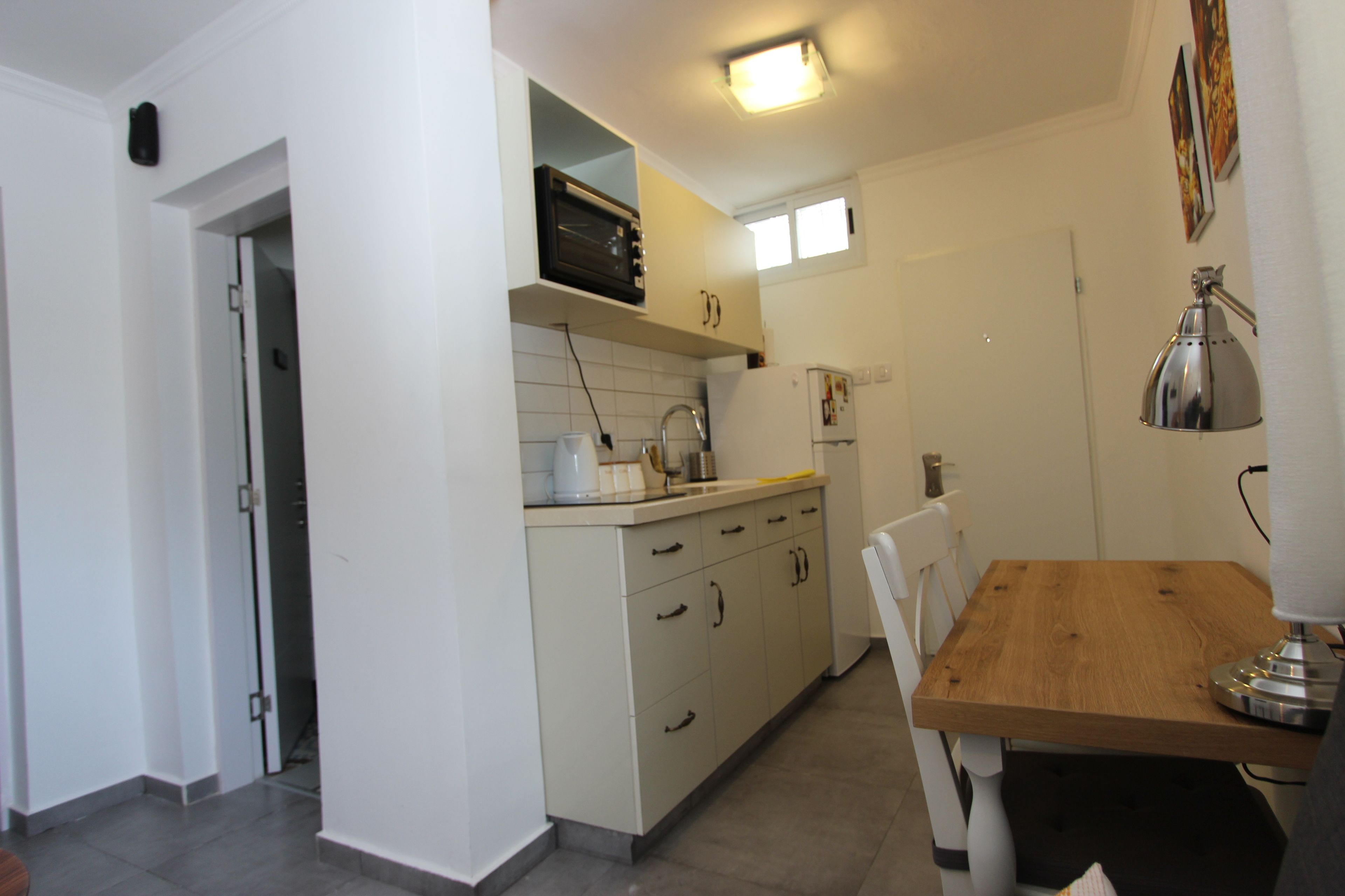 A compact kitchen with white cabinets, a wooden dining table, and a built-in microwave.