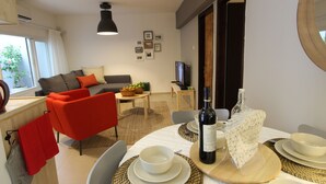 A dining area with a table set for four, a sofa, a television, and a window with curtains. - HaBaitBe Matityahu (Beersheba)