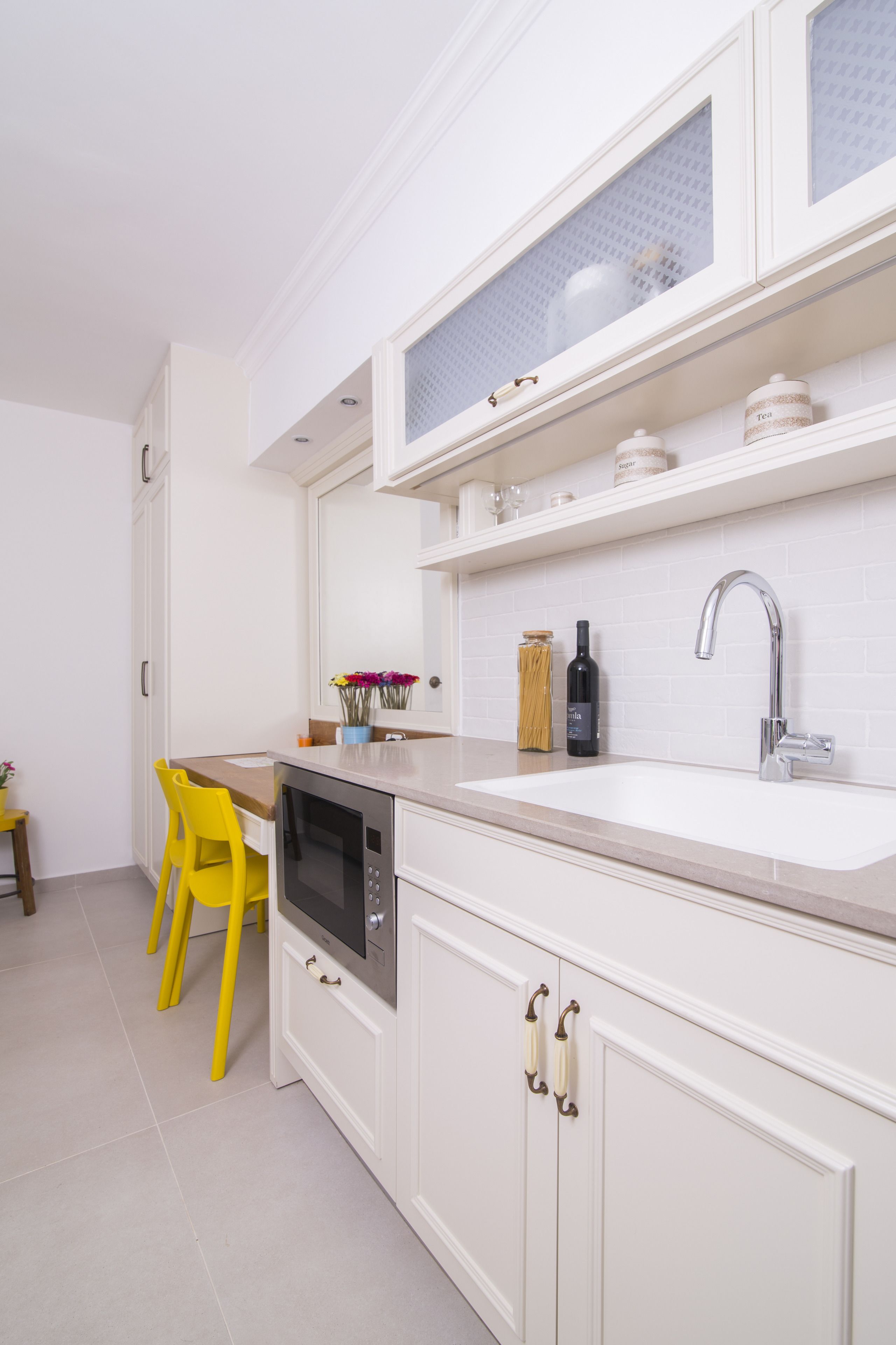 A modern kitchen with white cabinetry, a stainless steel oven, a sink with a faucet, and a yellow chair.