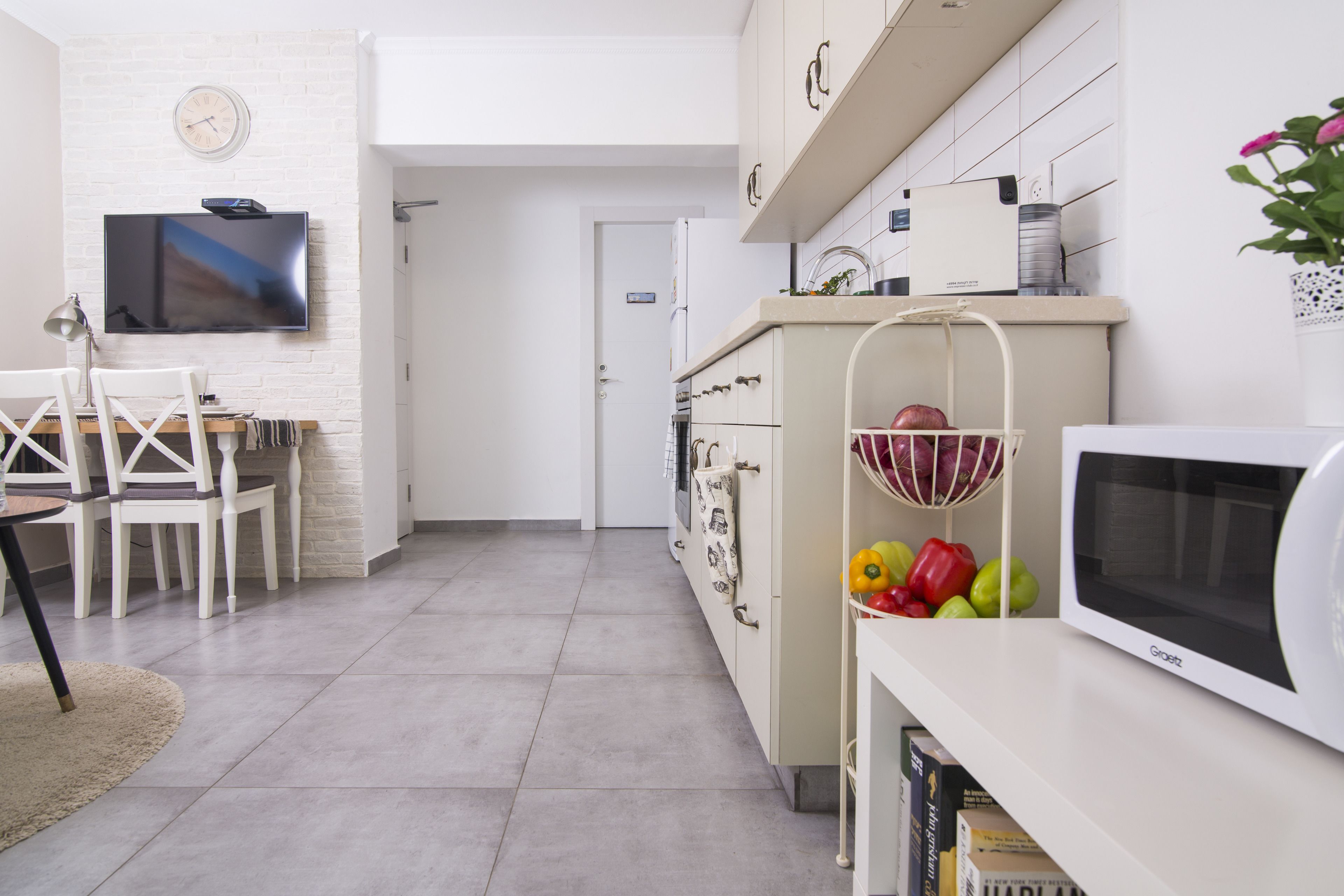 A modern kitchen with a flat-screen TV, white cabinets, and a microwave.