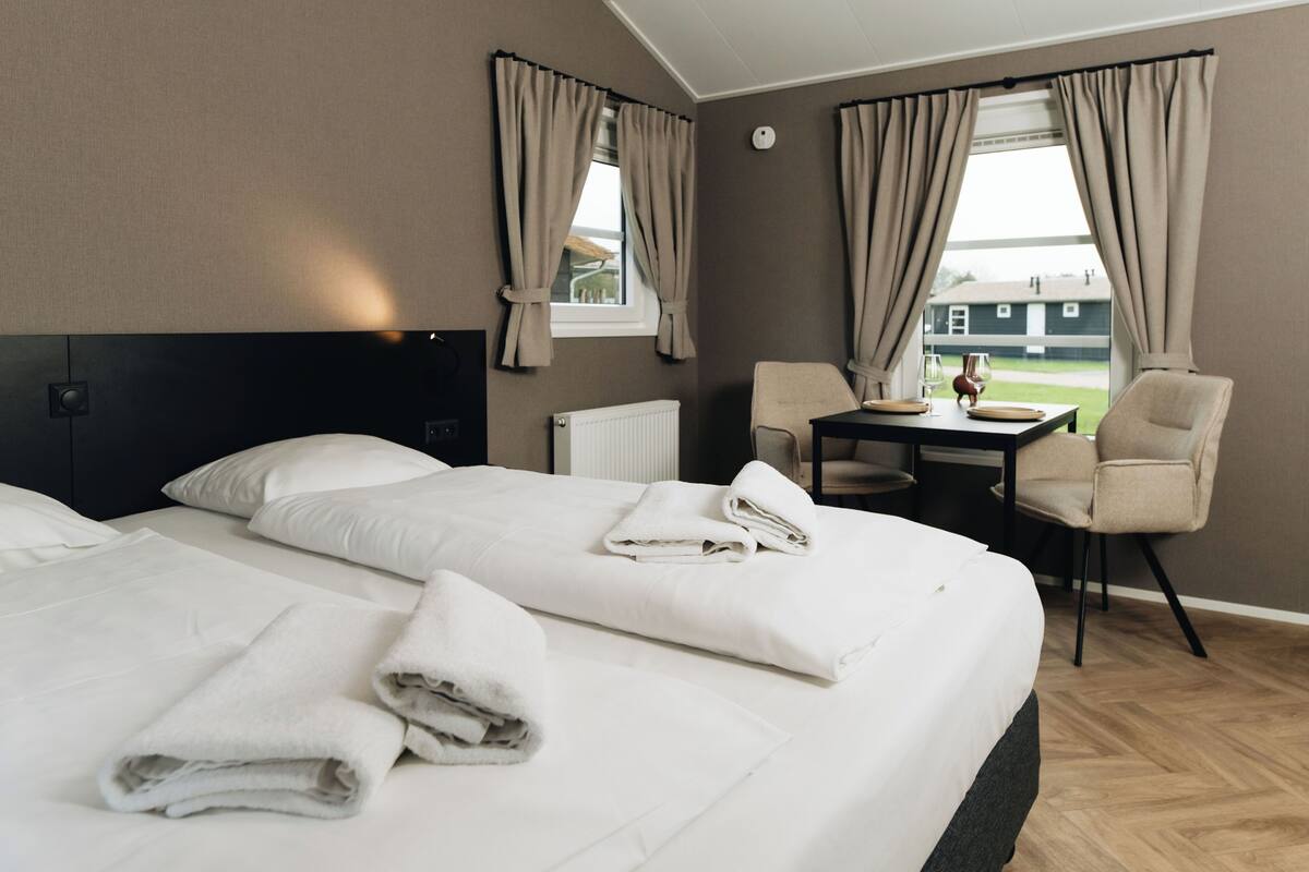A hotel room with a large bed, two chairs, a small table, and a window with curtains.
