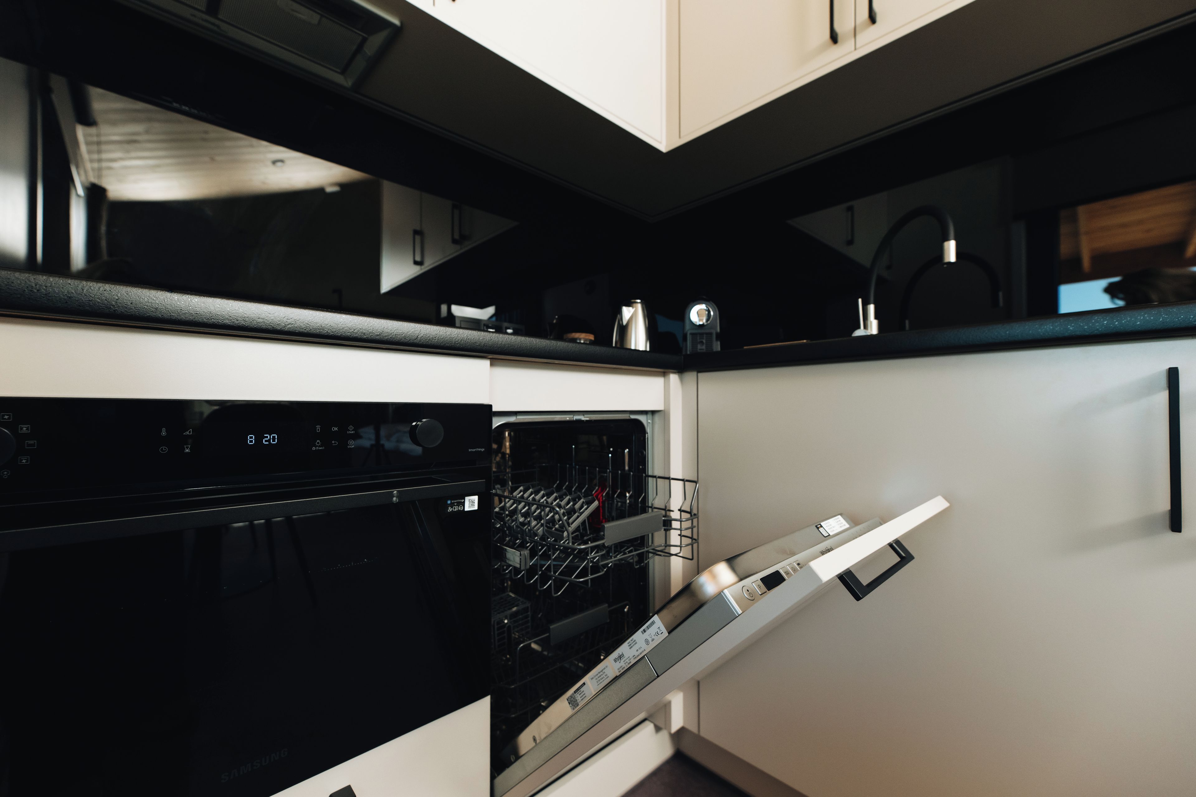 A modern kitchen with a built-in oven and dishwasher, white cabinetry, and a black countertop.