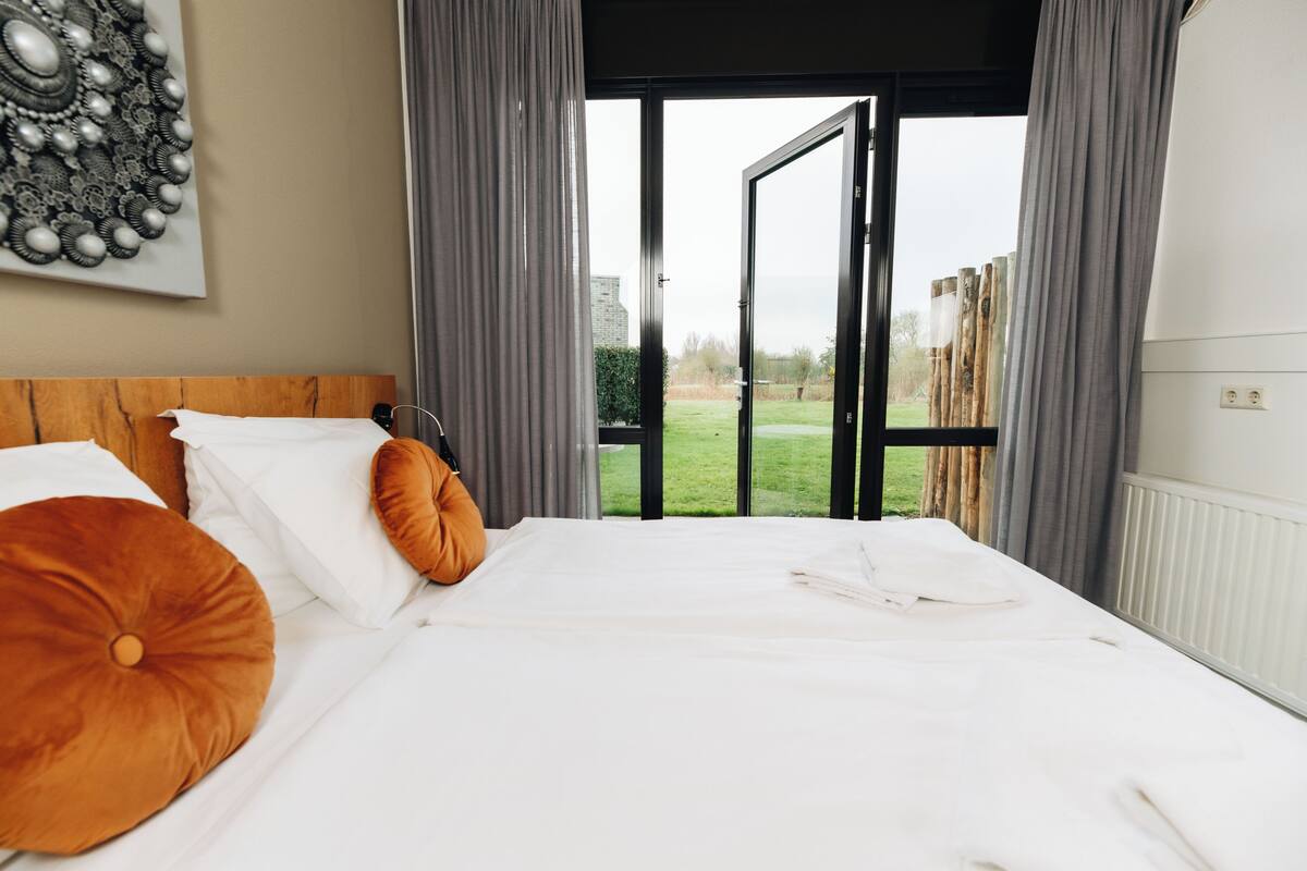 A bedroom with a large bed, a wooden headboard, and a view of a grassy area through an open door.