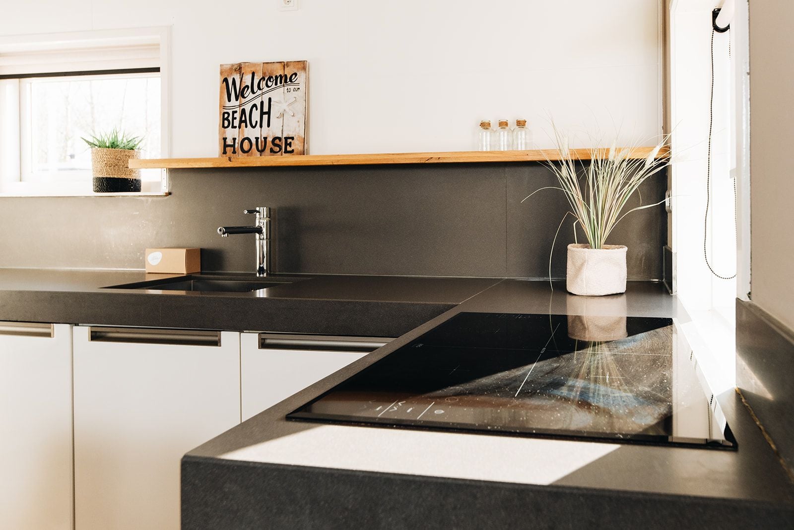 A modern kitchen with a black countertop, white cabinets, and a welcome sign above the sink.