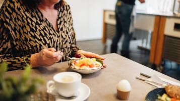Eine Person isst an einem Tisch, auf dem eine Schüssel Essen, eine Tasse Kaffee und ein Muffin stehen.