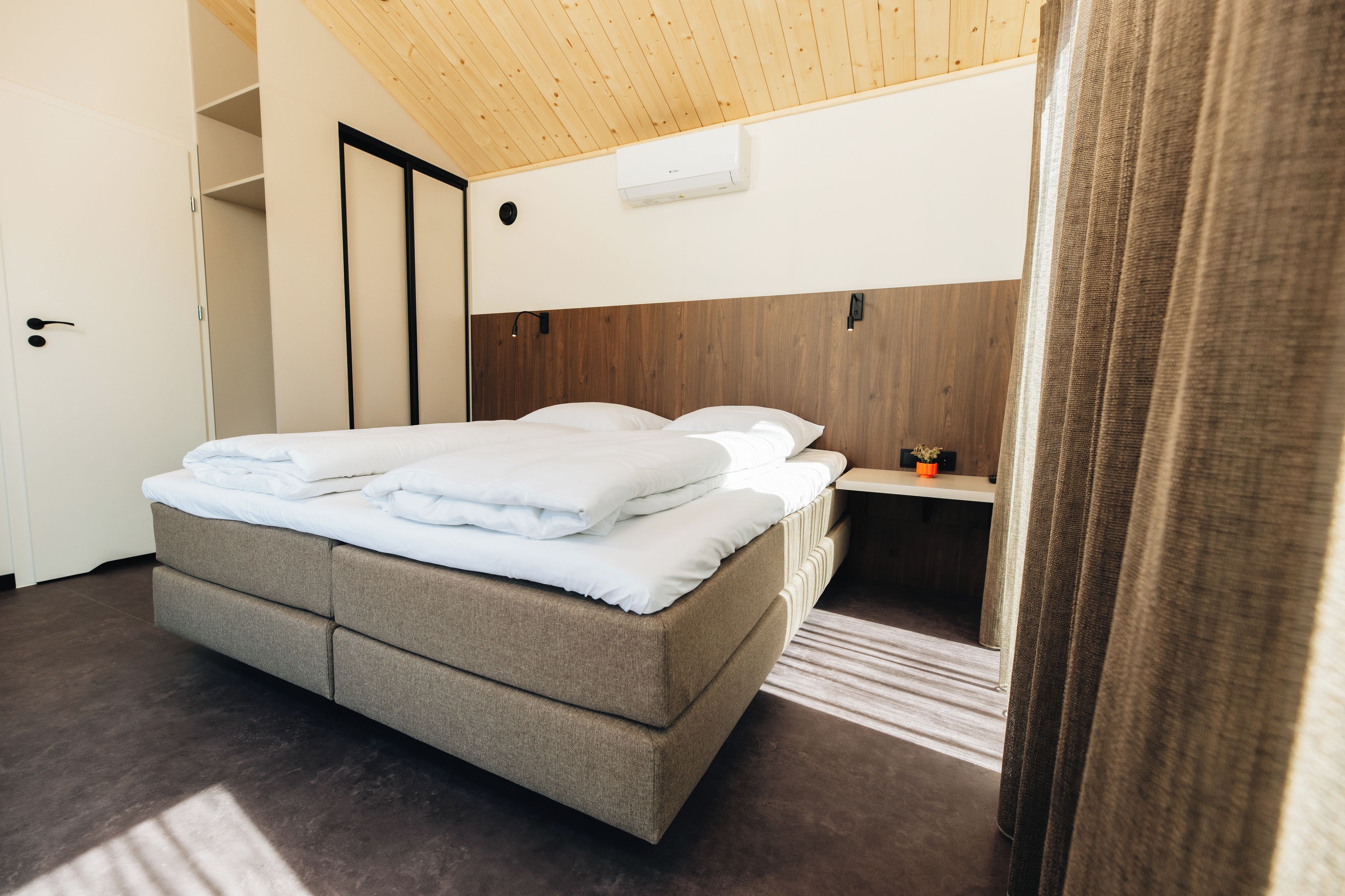 A modern hotel room with a bed, a small bedside table, and a wooden headboard.