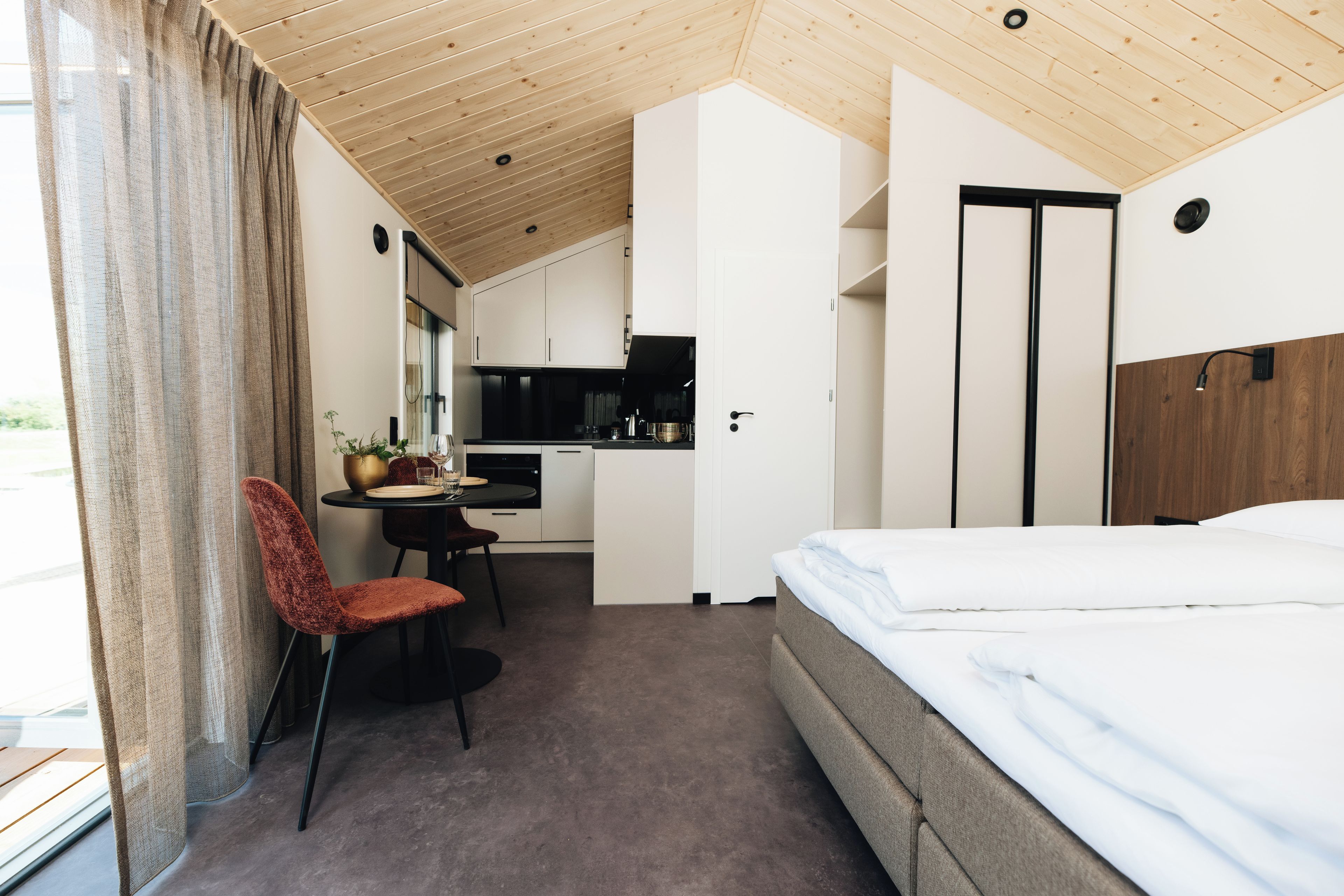 A compact hotel room with a bed, a dining table with chairs, a kitchenette, and a bathroom.