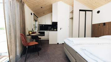 A compact hotel room with a bed, a dining table with chairs, a kitchenette, and a bathroom.