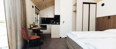 A compact hotel room with a bed, a dining table with chairs, a kitchenette, and a bathroom.