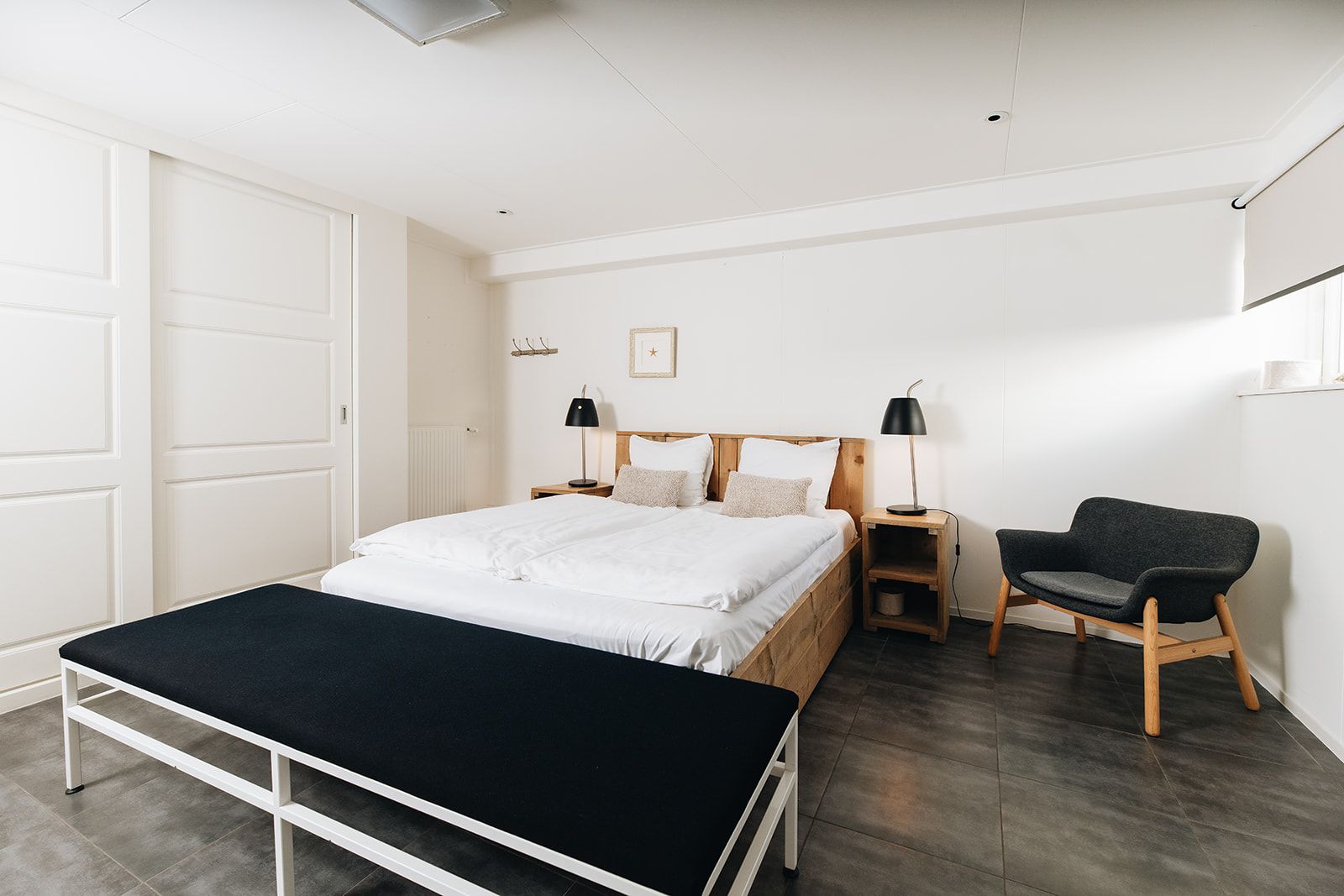 A bedroom with a bed, bedside tables, a chair, and a bench.