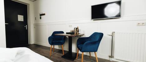 Ein Hotelzimmer mit Bett, Schreibtisch, zwei Stühlen, Fernseher und Heizkörper.
