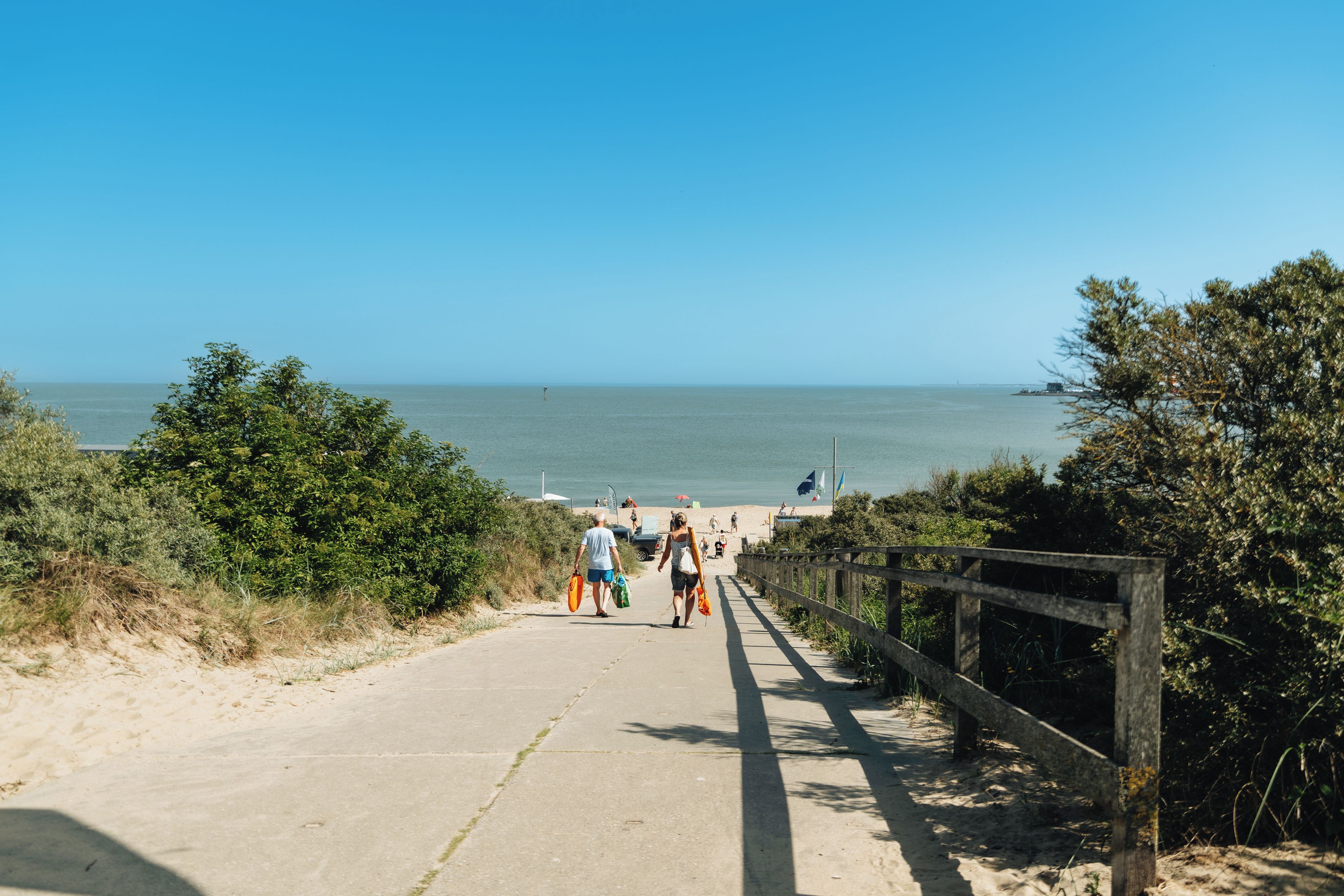 Un sendero pavimentado que conduce a una playa, con una valla de madera a un lado.