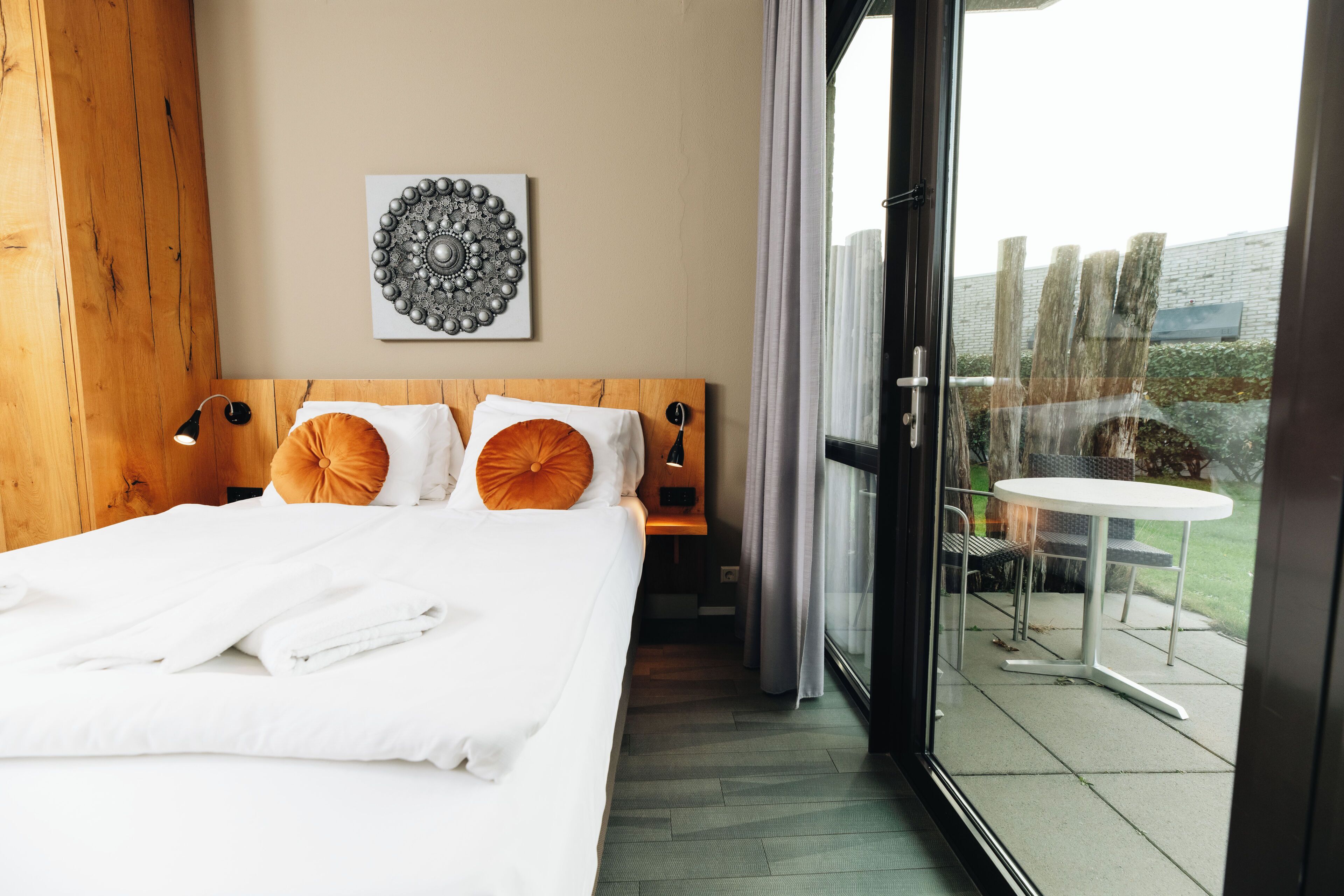 Una habitación de hotel con una cama grande, cabecera de madera, un plato decorativo en la pared y un balcón con mesa y sillas.