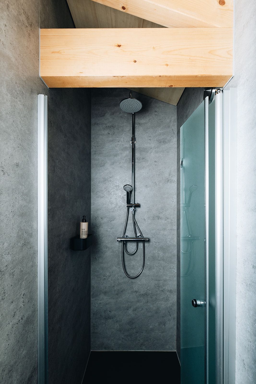 A modern shower with a wooden ceiling, a glass door, and a concrete wall.