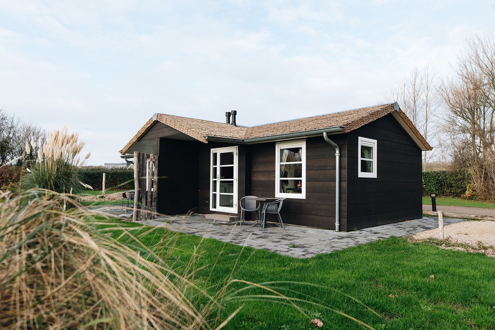 A single-story house with a dark exterior, a tiled roof, and a paved patio area.