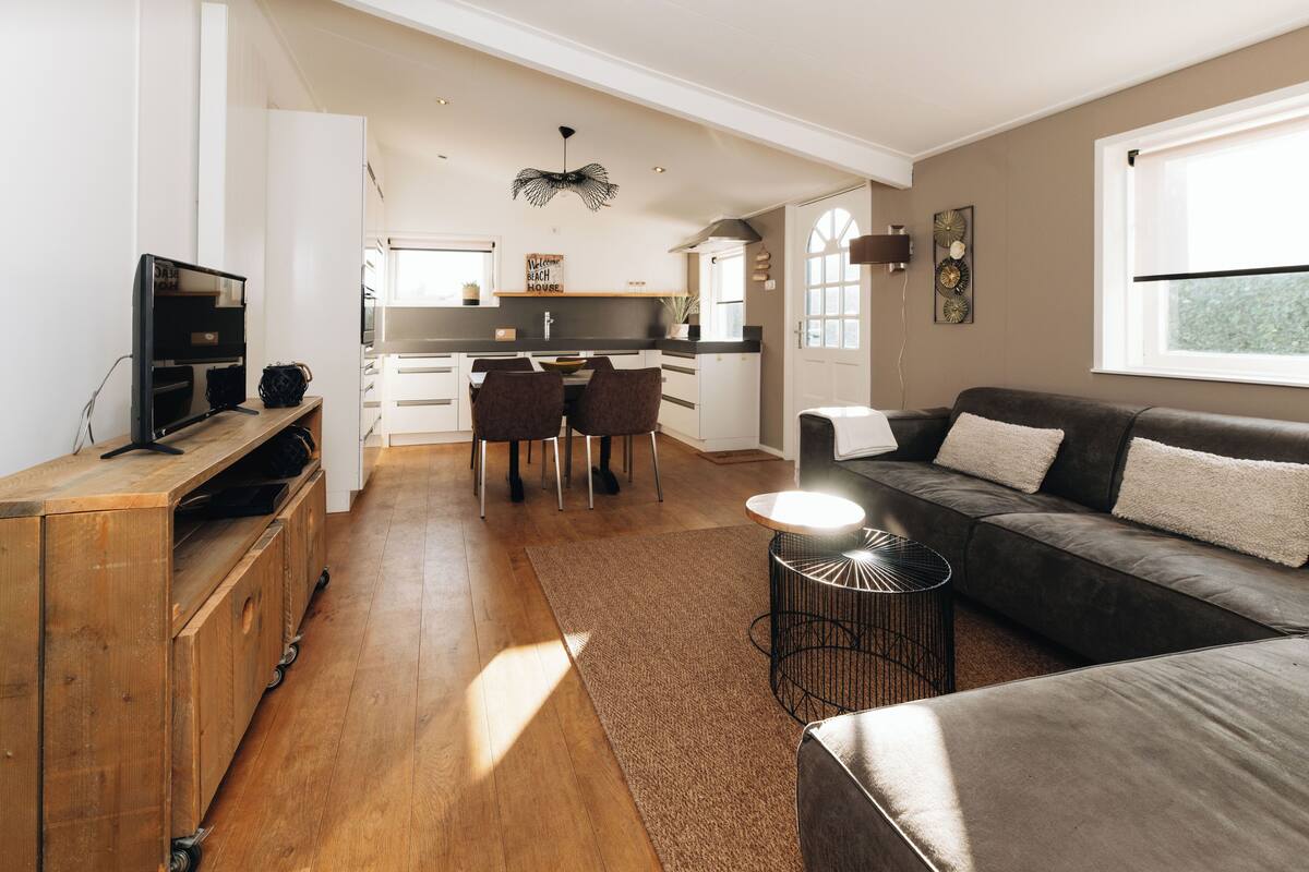 A modern kitchen with a dining area, a sofa, and a TV.