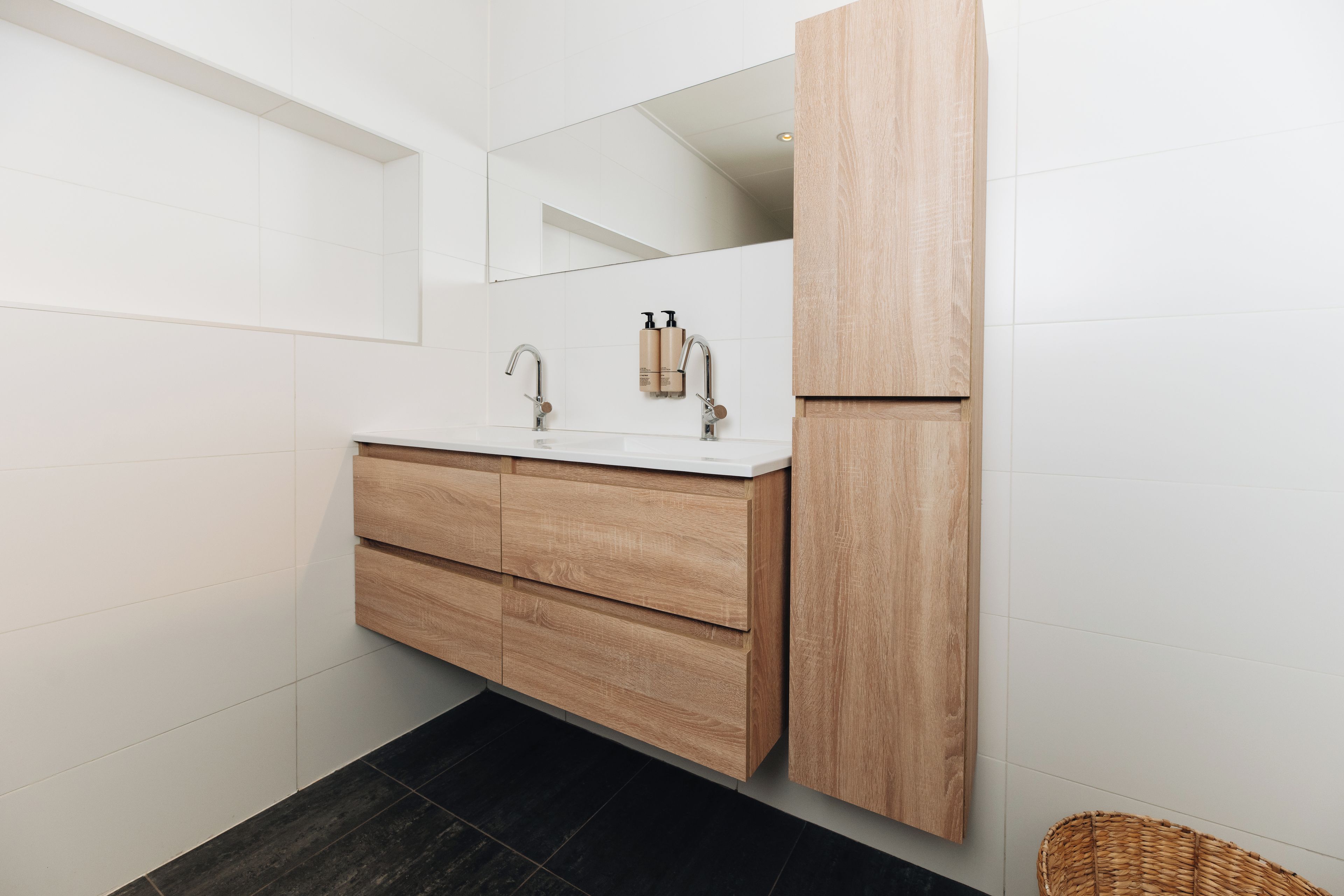 Ein modernes Badezimmer mit einem Holzbettchen, einem großen Spiegel und einem schwarzen Fliesenboden.