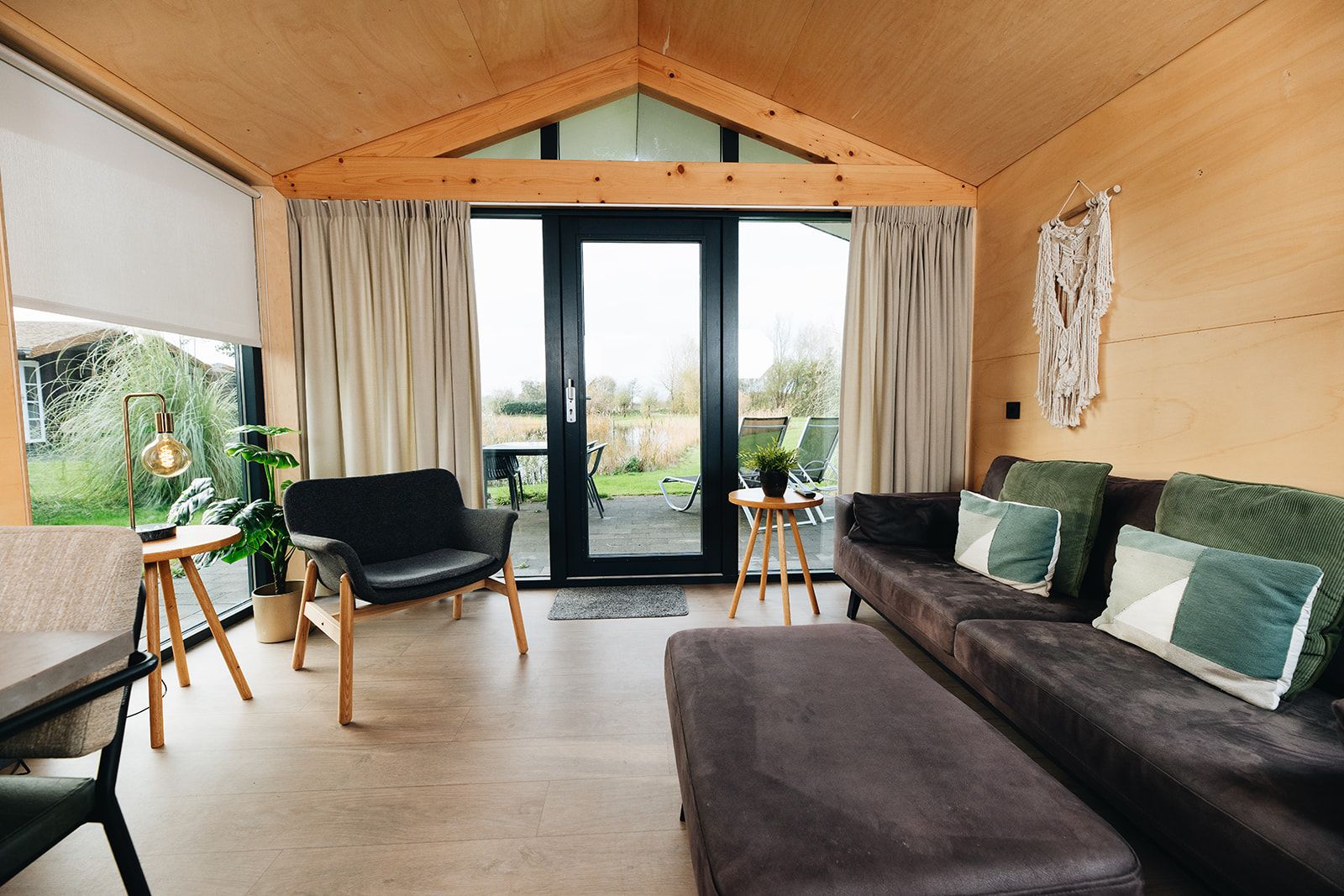 Un interno moderno con soffitto in legno, una zona con divano, una poltrona, un tavolino e una pianta in vaso.