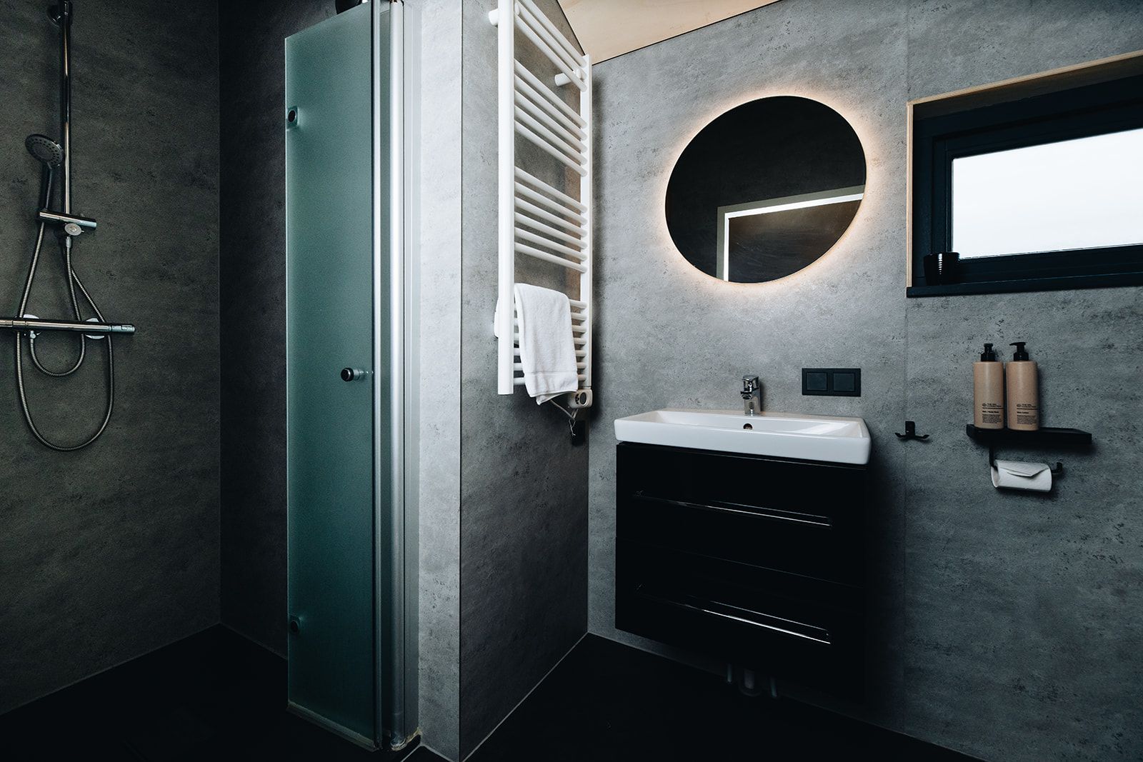 Une salle de bain moderne avec une douche à parois de verre, un lavabo blanc et un miroir rond.