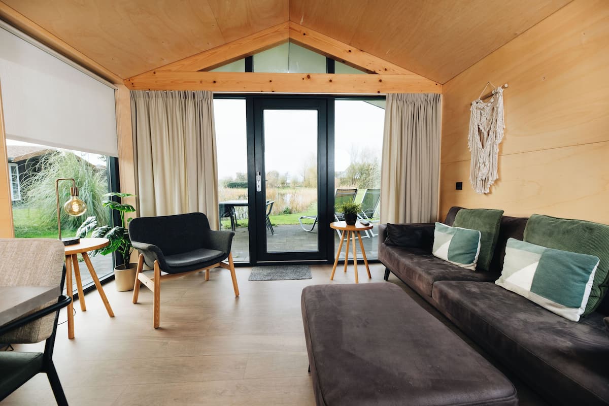 A modern interior with a wooden ceiling, a black sofa with green cushions, a black chair, a wooden table, and a potted plant.