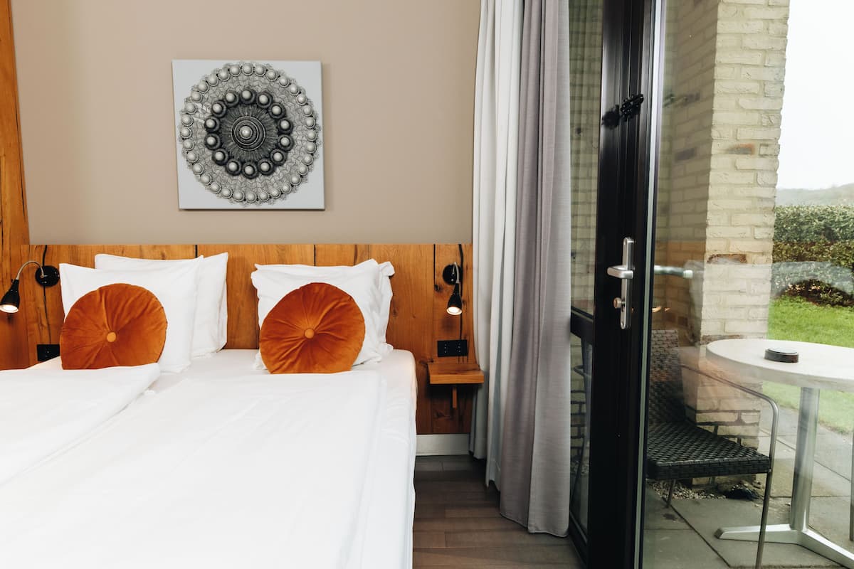 A hotel room with a bed, a wall-mounted artwork, a sliding glass door to an outdoor area, and a small table.