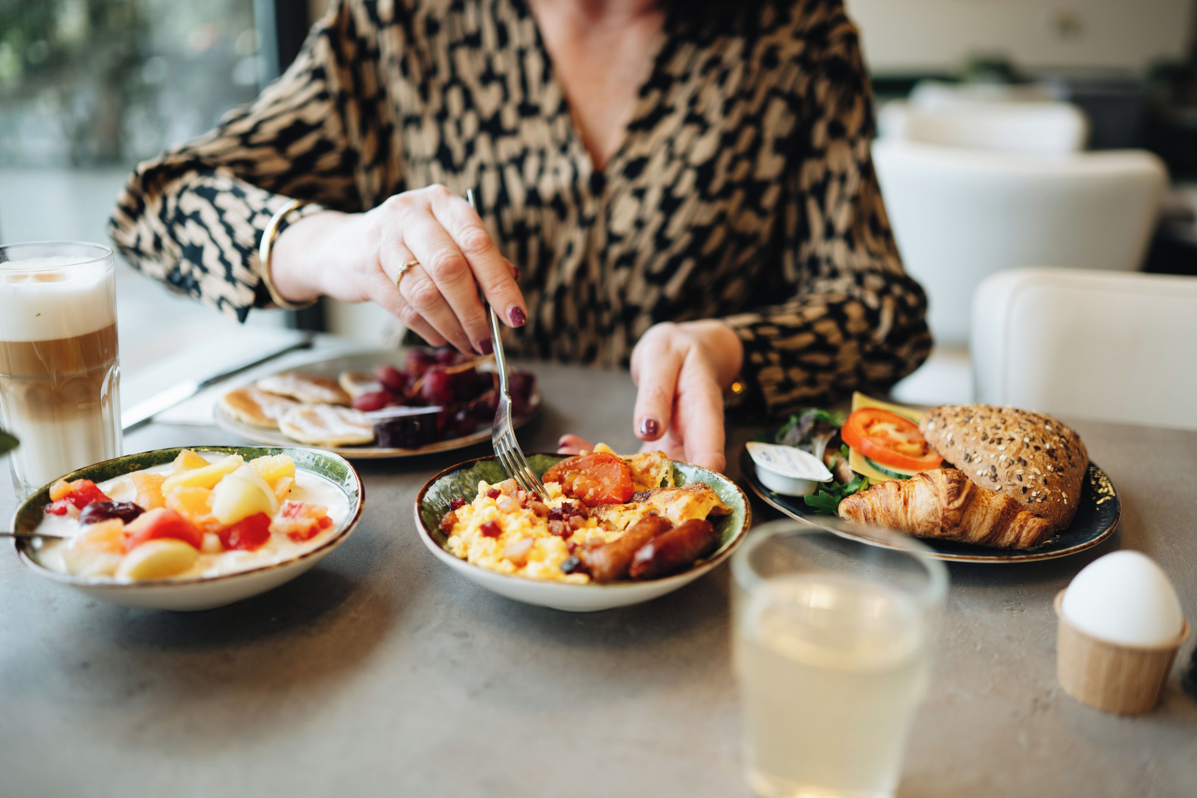 A person dining at a table with various food items including a croissant, salad, and fruit.
