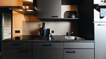Una cocina moderna con cafetera integrada, un lavamanos y una pequeña planta en maceta sobre la encimera.