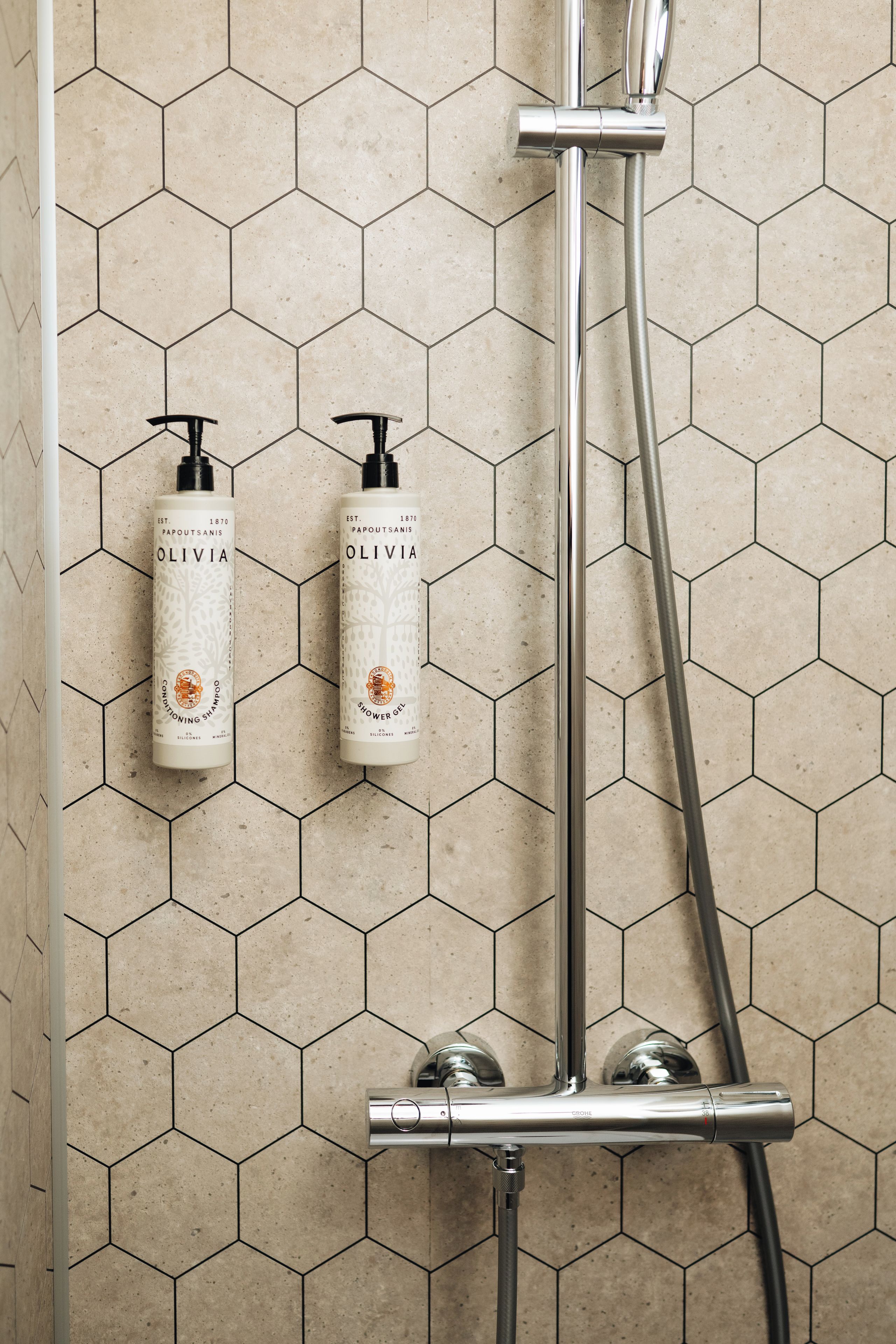 Un baño con baldosas hexagonales, una ducha y dos botellas de gel de ducha Olivia.