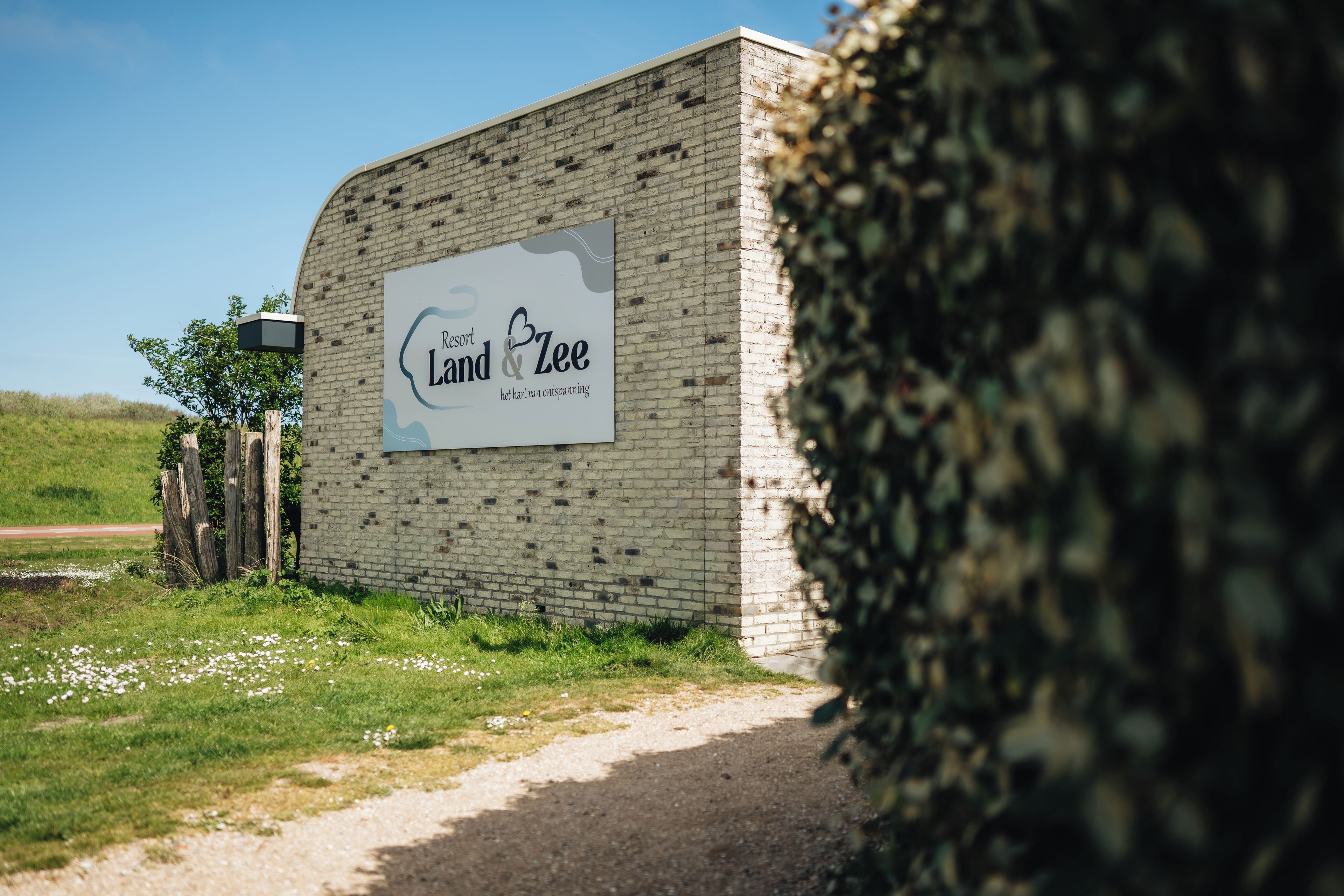 Un muro in mattoni con un cartello che indica 'Resort Land & Zee' e un vialetto che vi conduce.