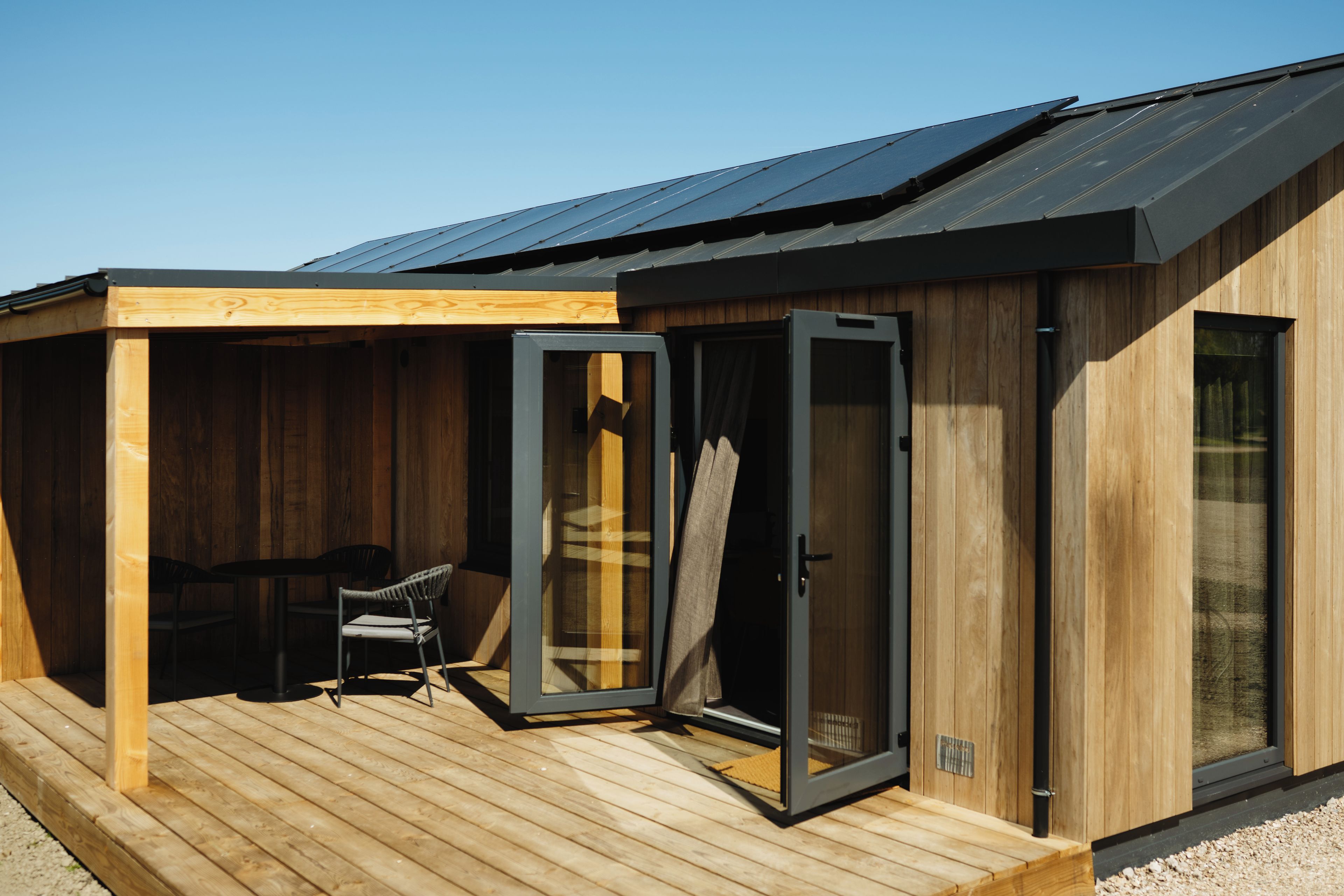 A wooden cabin with a deck, a sliding glass door, and a chair.